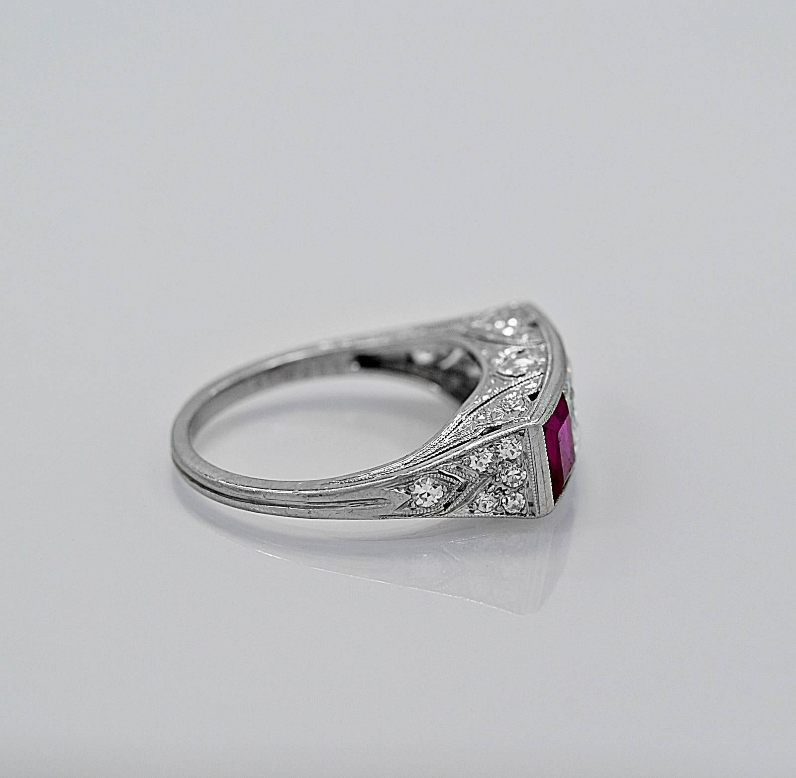 A geometrically tailored Art Deco ruby and diamond engagement ring with an accompanied A.G.L. cert. It features 2 Burma rubies that are unheated and weigh .75ct. apx. each that are set on each side of an emerald cut center diamond. This