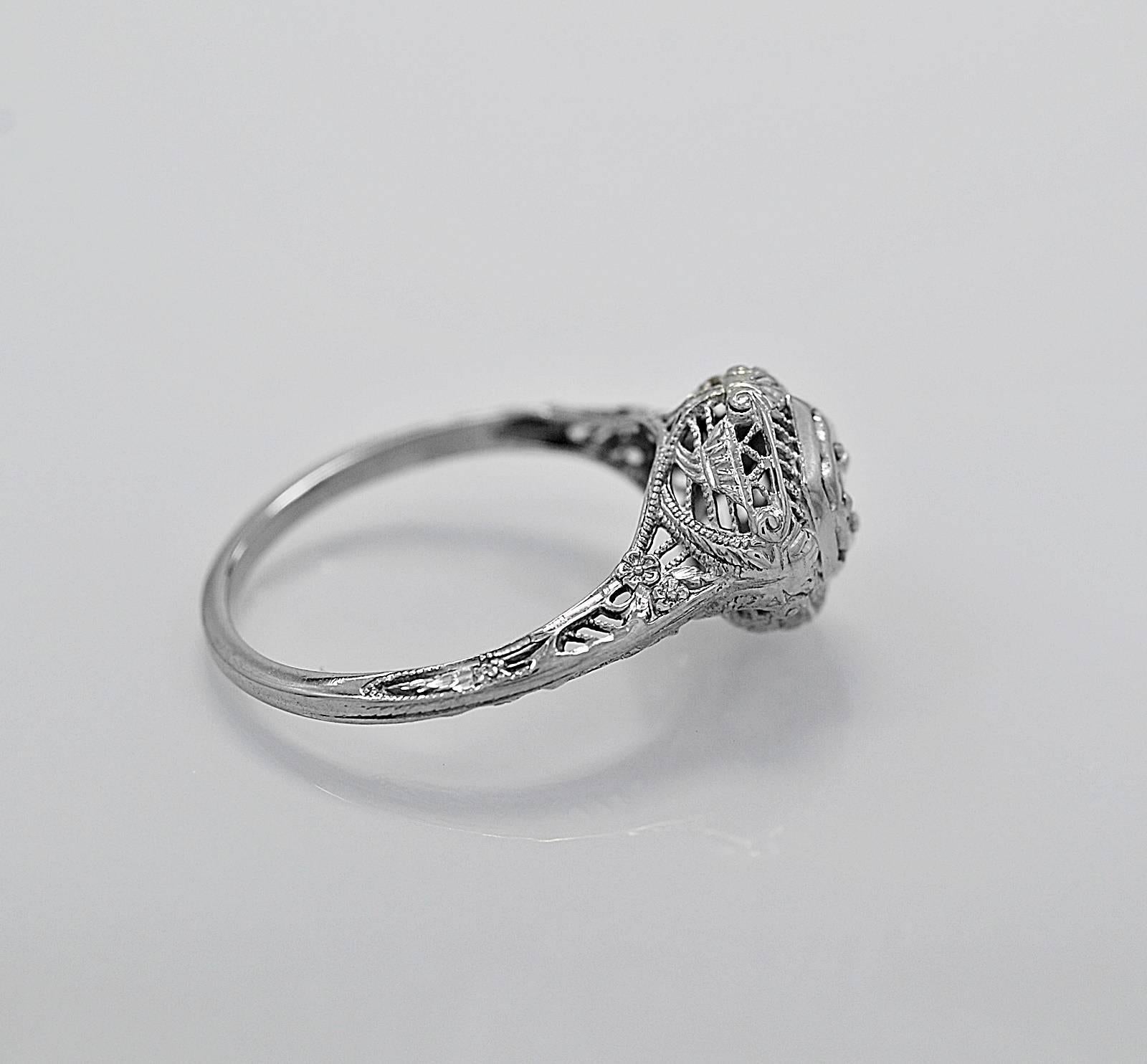 A meticulously filigreed antique engagement ring crafted in 18K white gold and features a .10ct. apx. transitional cut center diamond with VS2 clarity and G color. Notice the filigree surrounds the diamond, completes the gallery and moves down the