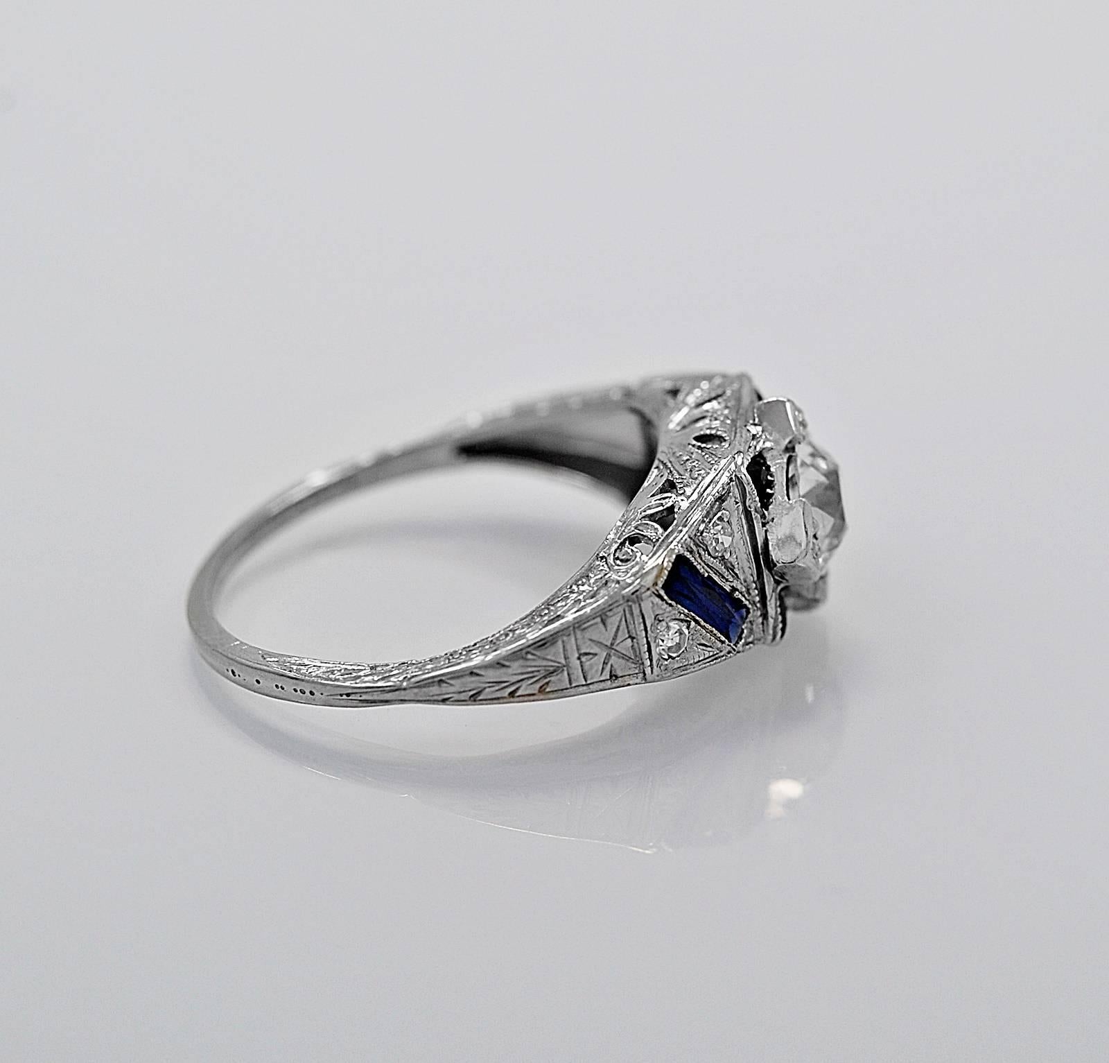 A gorgeous antique engagement ring featuring a .60ct. apx. European cut center diamond with VS1 clarity and I-J color. It is accented with .08ct. apx. T.W. of sparkling single cuts and .50ct. apx. T.W. of synthetic sapphires. The center diamond is