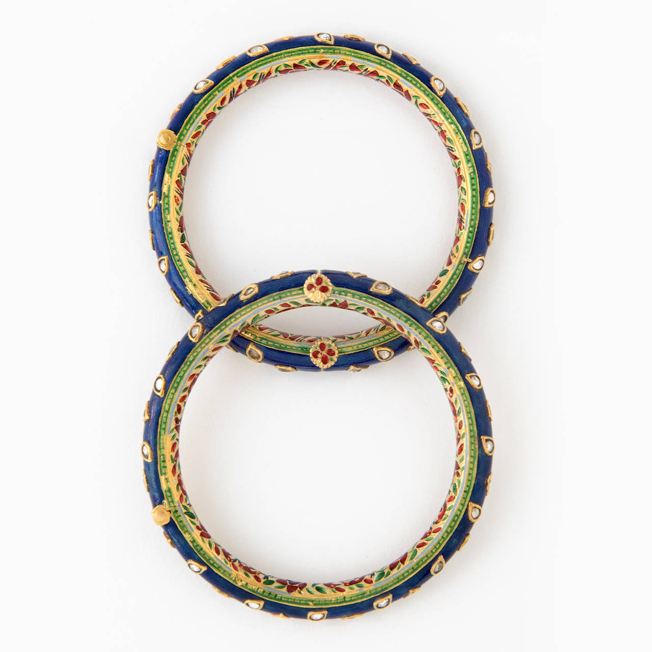 A pair of gold bangles, CHURIN, of which the outer side is decorated with dark blue, Nil Zamin enamel, kundan set with white sapphire in gold collets, shaped like leaf and flower buds. The inside is decorated in a floral pattern with Safed Chalwan