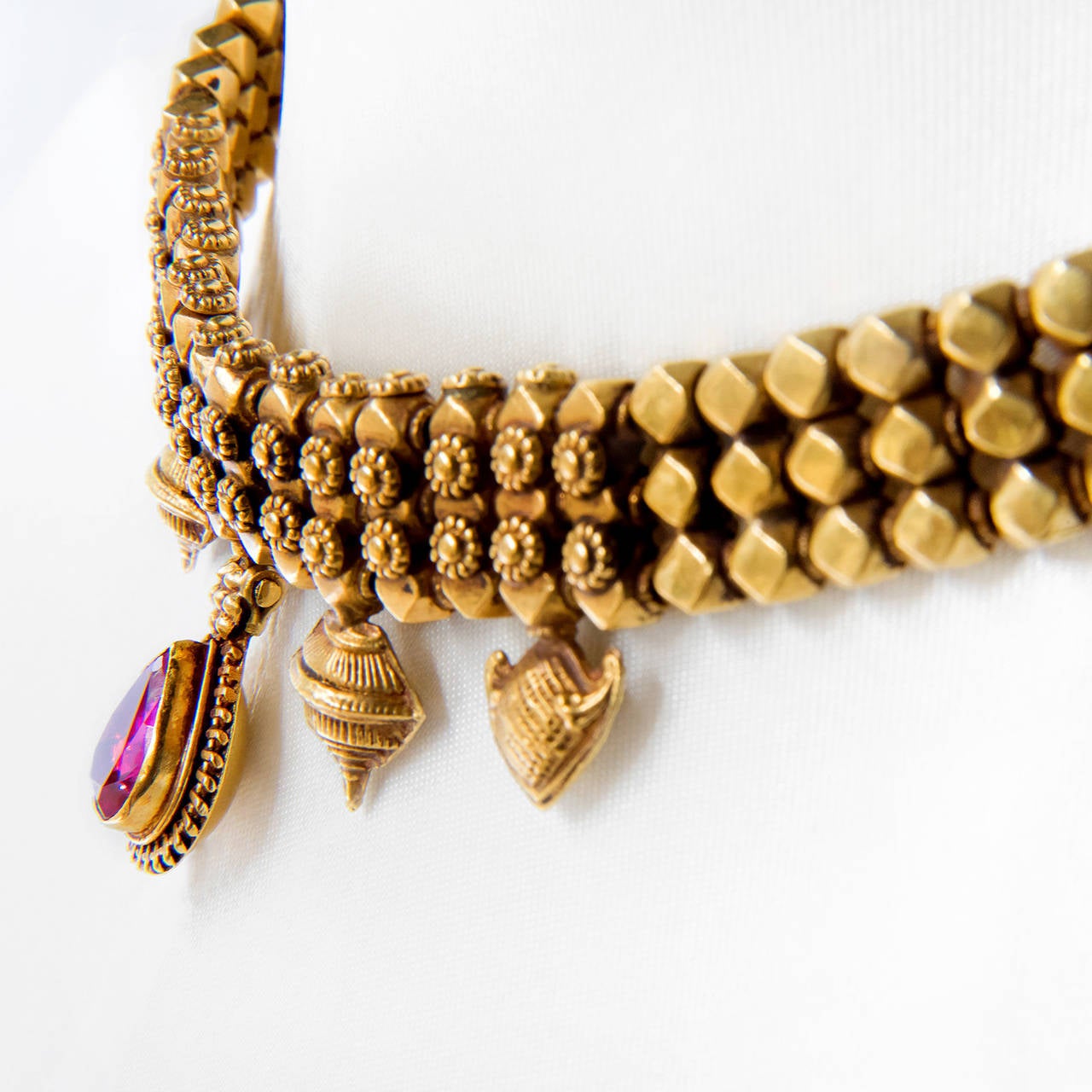 A gold necklace with a central almond shape drop, kundan set with red glass, flanked by two suspended hindu emblems on either side. The finials of the necklace have an embossed decoration of Kirtimukha.

India, Maharashtra, early 20th century