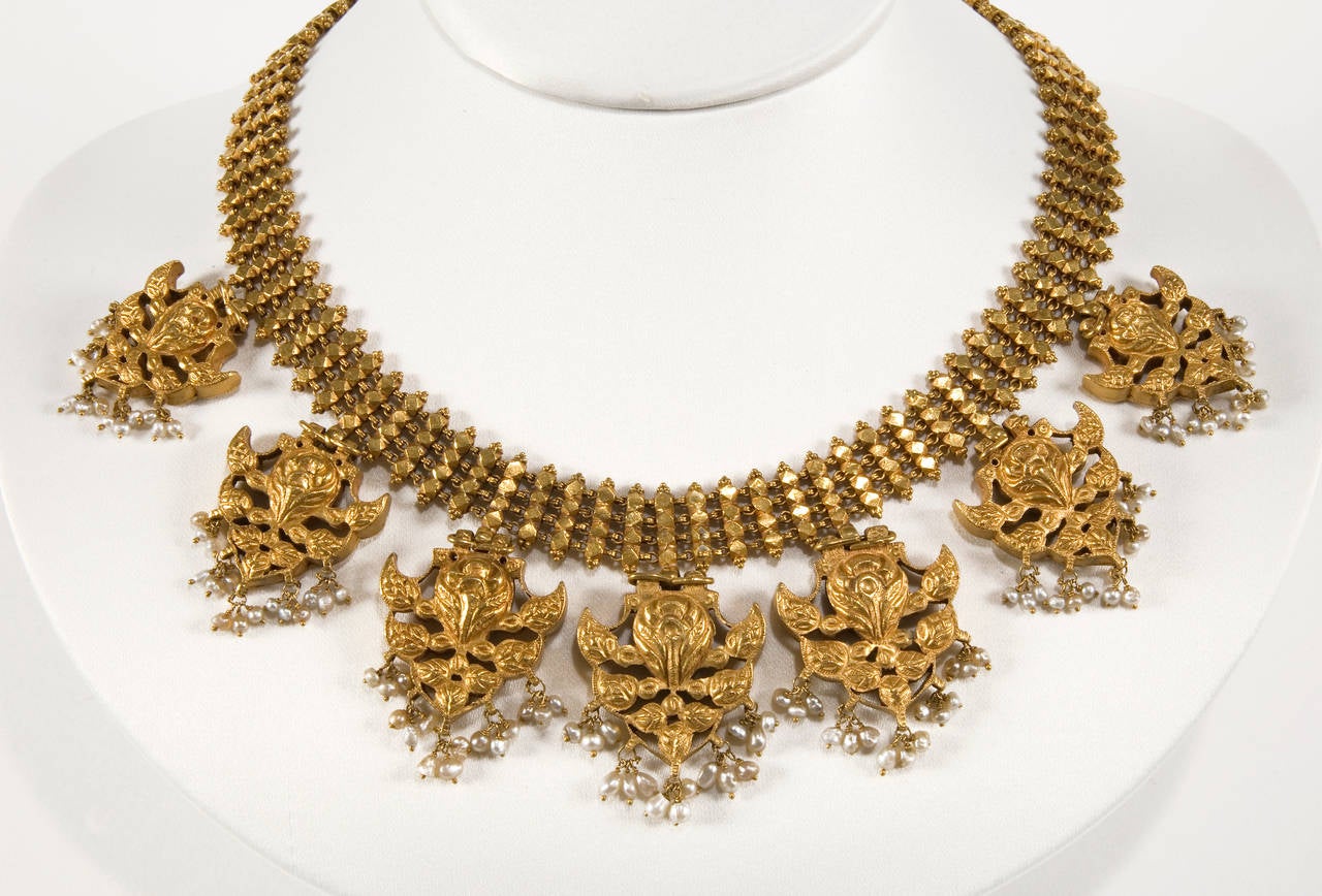 A necklace, consisting of seven minutely worked gold pendants, hung from a gold chain of linked vertical, polygonal units. Each pendant has an open worked, stylized arrowhead shape, set with diamonds and alternately rubies, spinel, almandine, and