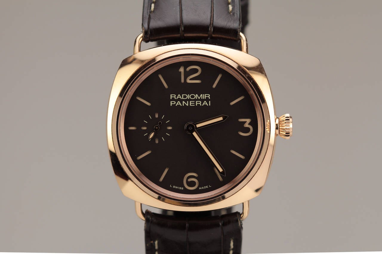 This is a Panerai rose gold Radiomir. This has a cushion shaped case with a exhibition back exposing  the manual wind movement. It is on a Panerai leather strap with a Panerai tang buckle.