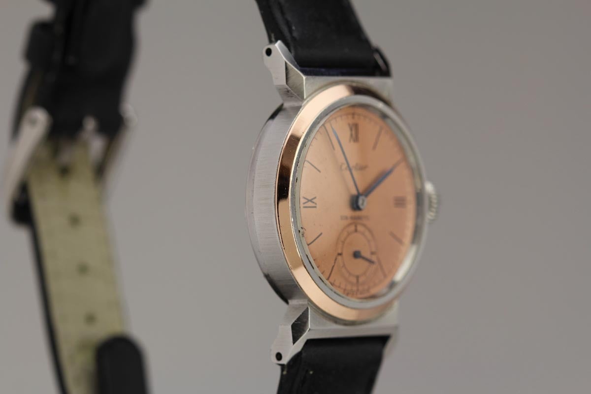 Movado Retailed by Cartier in stainless steel with rose gold plating. c. 1940s

A rare watch in the Cartier signed dial version and made by Movado. This has an rose dial with Roman numerals and rose gold bezel. The case has covered lugs with very