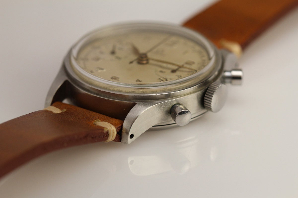 This is a mint example of a 1940s Omega Chronograph in stainless steel with a mint original dial. This is an oversize chronograph measuring 38mm. This Omega is a reference 2077-1 and has the highly collectible 33.3 manual wind Omega caliber.