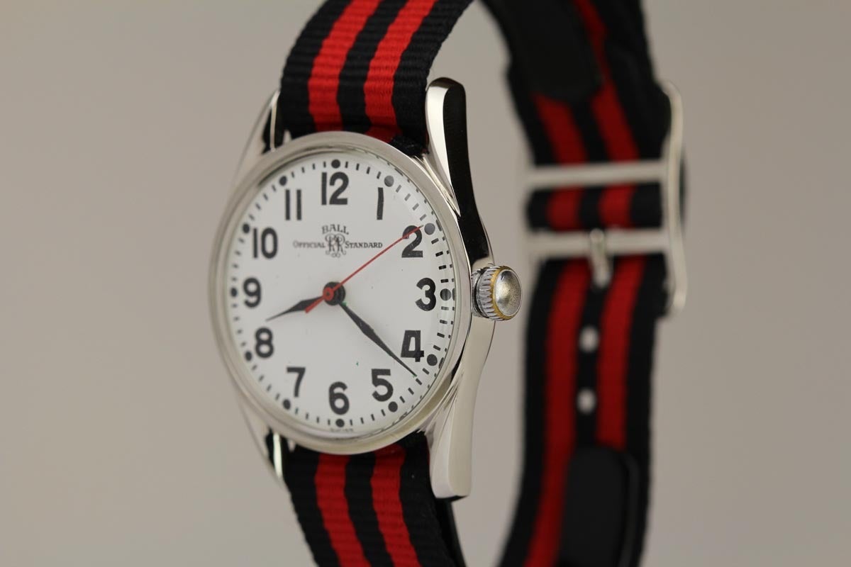 Ball Official Standard Railroad wristwatch with a manual wind movement, round screw back case, white dial, painted black Arabic numerals, black feuilles fortes hands, red center sweep second, plastic crystal, smooth bezel, black/red nylon strap,
