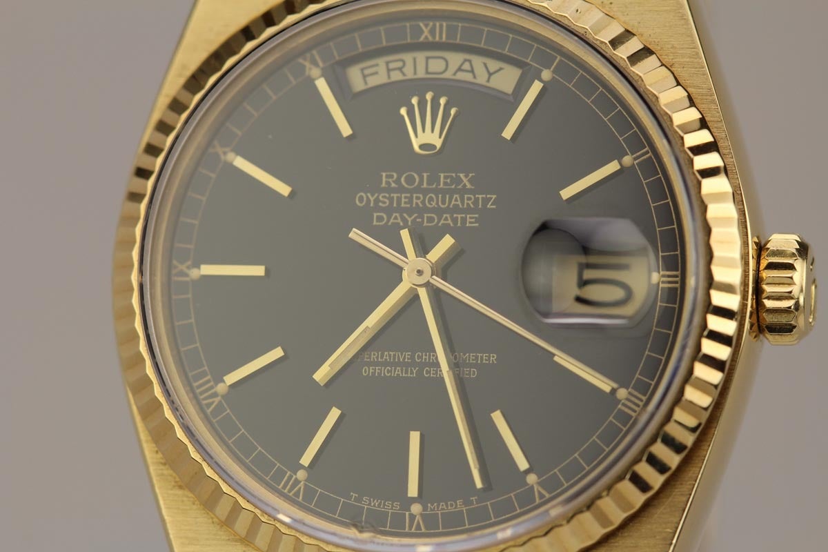 Rolex Day-Date Quartz Ref 19018 with a black gilt dial, sapphire crystal, fluted bezel, and integrated Rolex gold bracelet with deployant clasp.