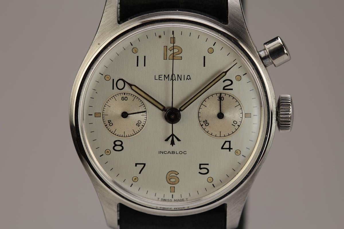 This Lemania stainless steel military wristwatch with Broad Arrow on dial, from the 1950s, 38mm. This has a manual-wind movement, single-button chronograph, the screw down back case has the military markings, and is on a modern nylon military strap.