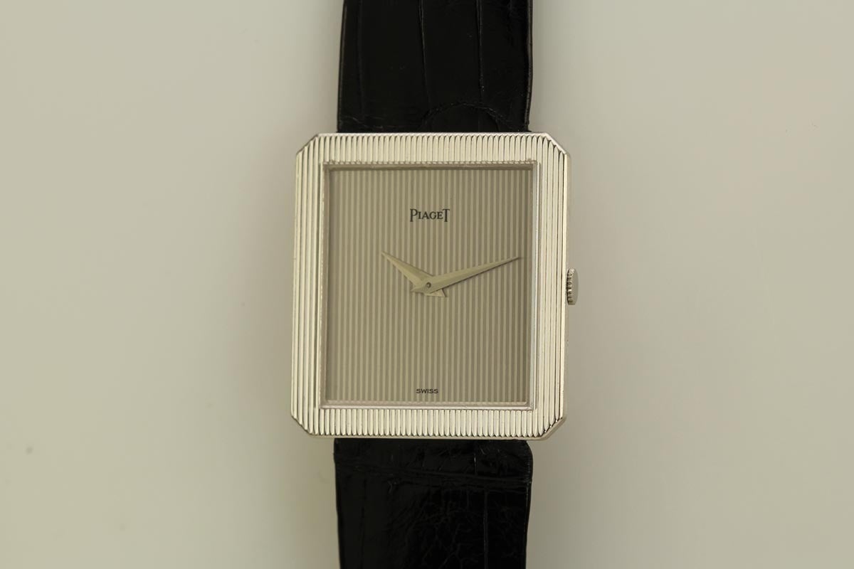 Piaget 18k white gold Protocole wristwatch, P 9154 movement, textured bezel, hooded lugs, sapphire crystal, manual-wind movement, on a black Piaget leather strap with a white gold tang buckle.
