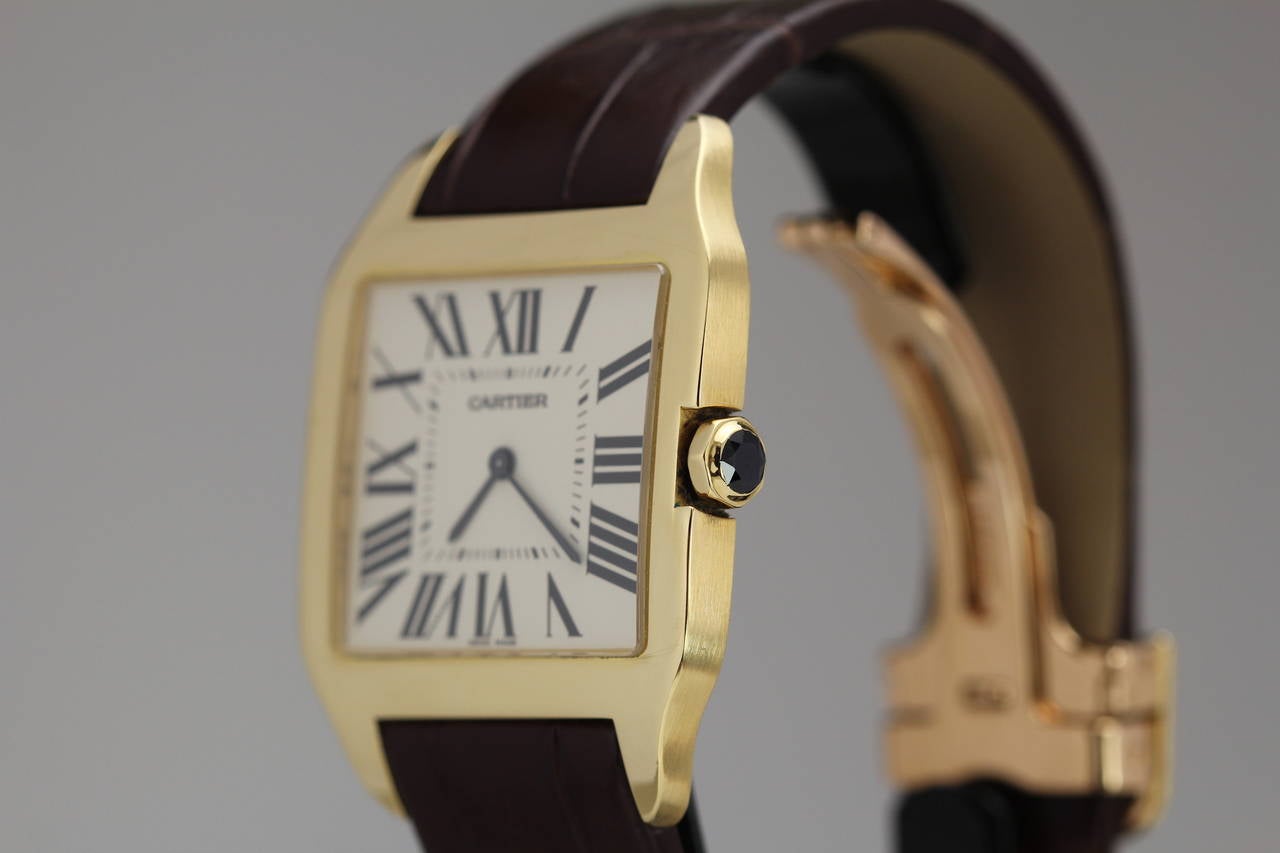 This is the Cartier Santos with a manual-wind movement, white matte dial, Roman numerals with secret signature at VII, blued steel hands, faceted sapphire-set crown,  and is on an 18k yellow gold Cartier deployant clasp and a new Cartier strap.