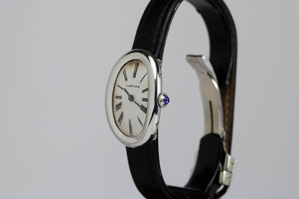 Classic Cartier Baignoire lady's wristwatch with an original dial, Roman numerals, blued steel hands, curved oval platinum case with hidden lugs on a leather strap and deployant Cartier clasp.

According to today's fashion we would consider this