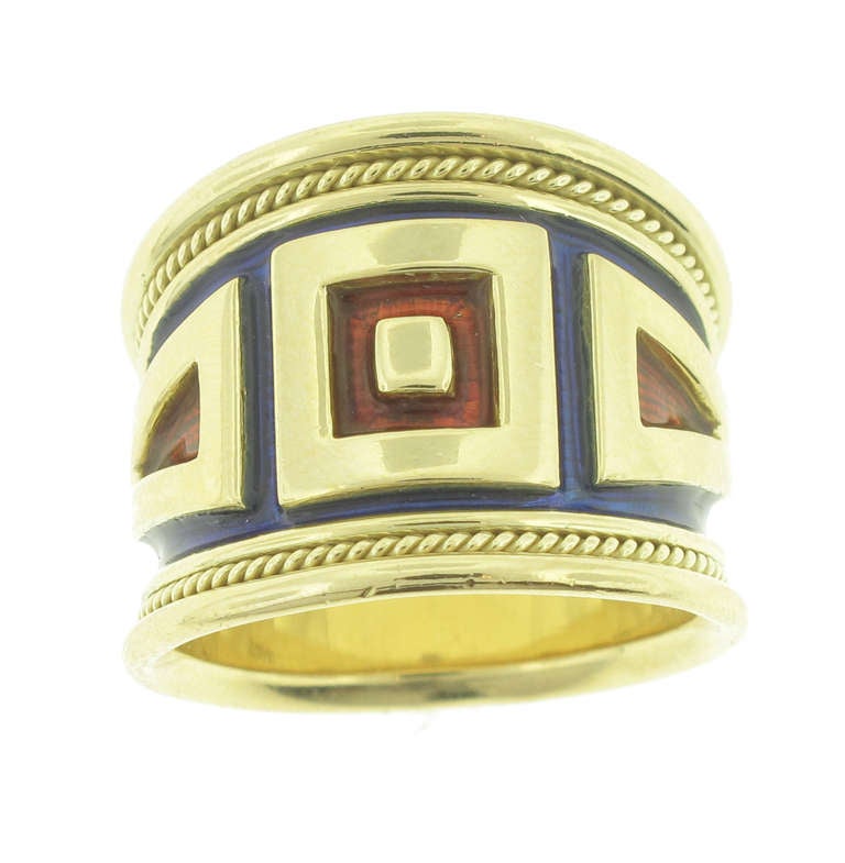 This Elizabeth Gage Wide Gold and Enamel Ring features blue and red enamel and is 18 karat yellow gold. The ring is a size 7 and is 17 millimeters wide at the widest section (the front) and tapers down to 10 millimeters and the thinnest section (the
