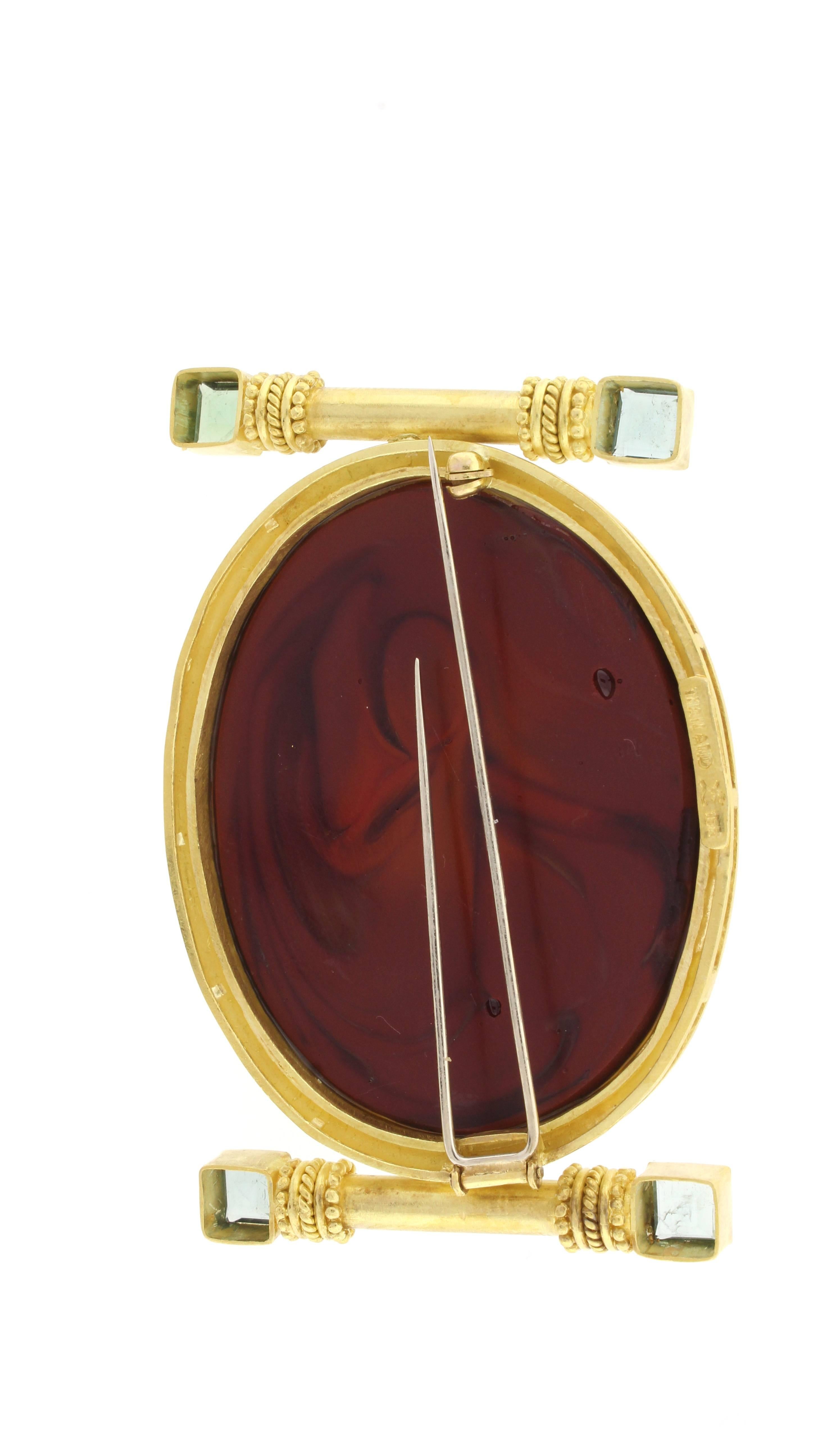 From acclaimed jeweler, Elizabeth Locke this 19 Karat carved burgundy glass  cameo brooch depicting  the head of medusa of Greek mythology. The oval cameo measures 1 ½ by 2 ¼ inches.  The cameo is set in a heavy gold border supported by to gold