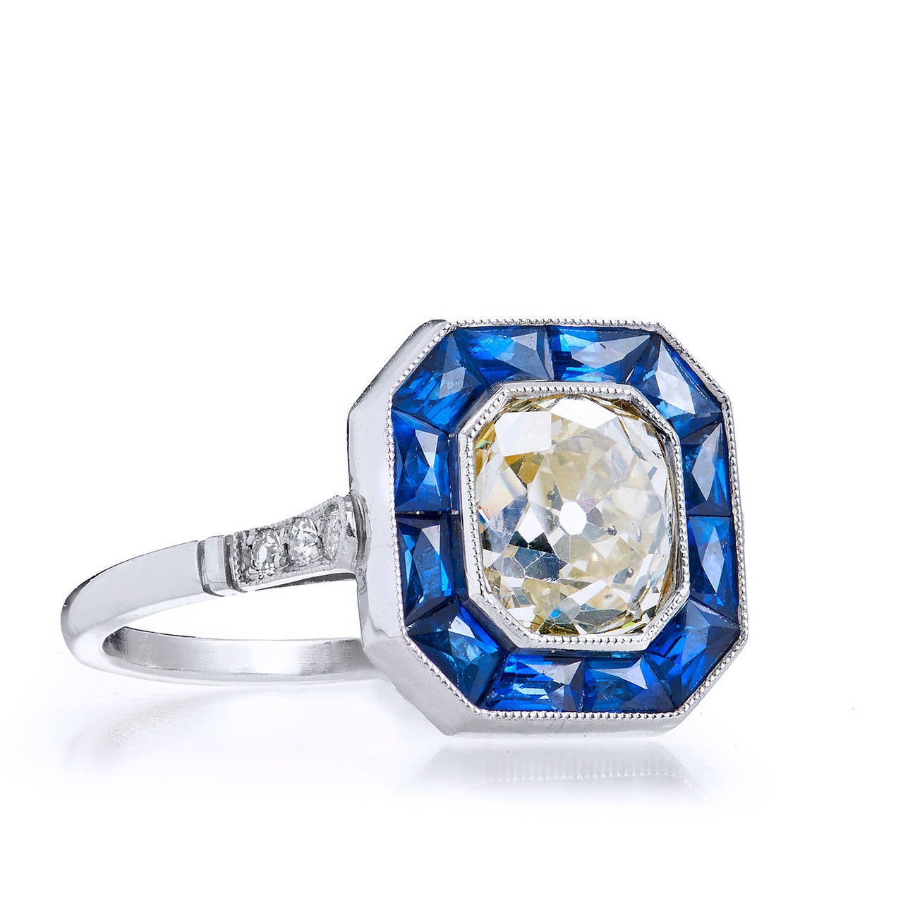 This picturesque ring captures the target design flawlessly with channel set French cut sapphires framing the 1.63 carat old mine very light brownish yellow diamond as the focal point  of the jeweled canvas. The ring is complete with diamonds set