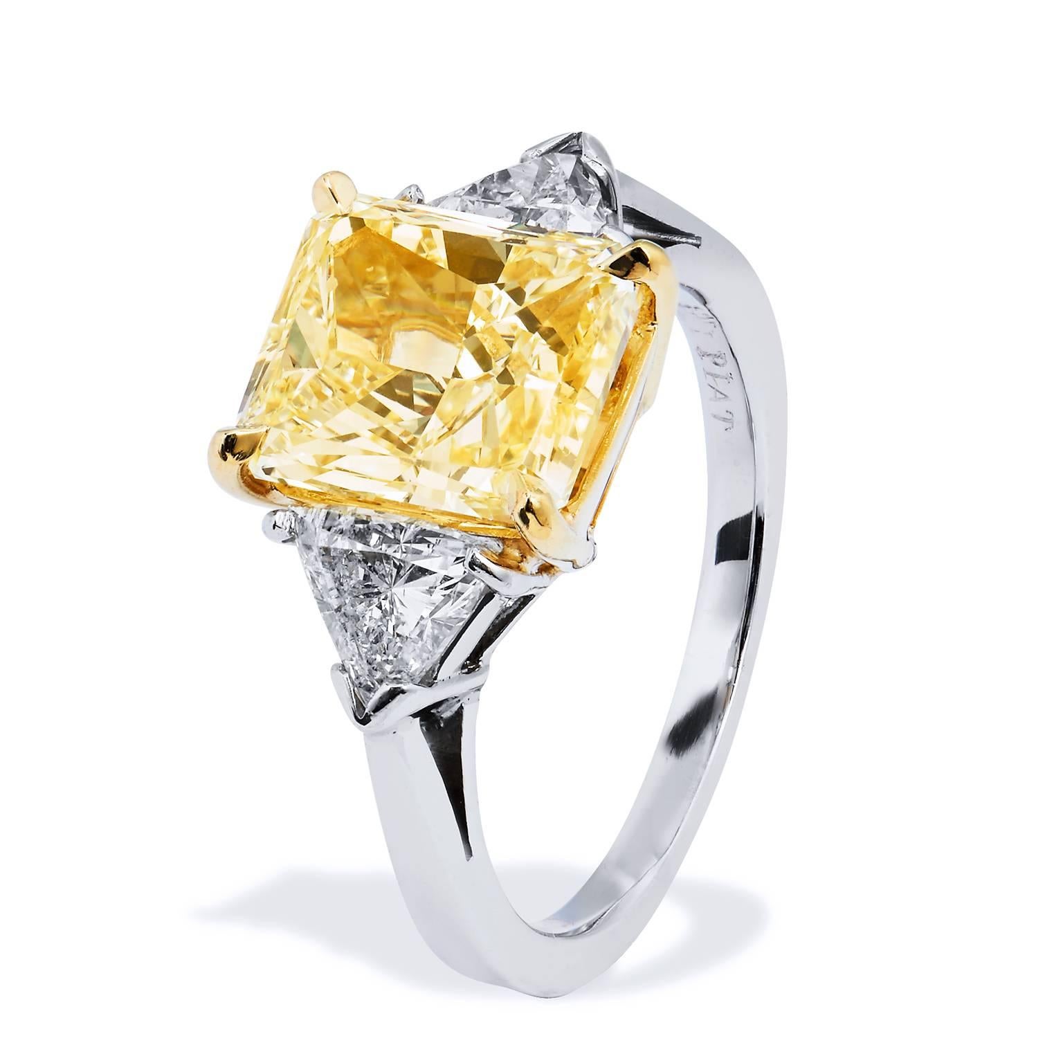 An engagement ring that will set her heart ablaze. An extraordinary 3.60 carat fancy yellow diamond set at center in 18 karat yellow gold from bridge to gallery, smolders with a bold, rich glow (W/S2; GIA #2101082871).  Two pieces of trillion cut