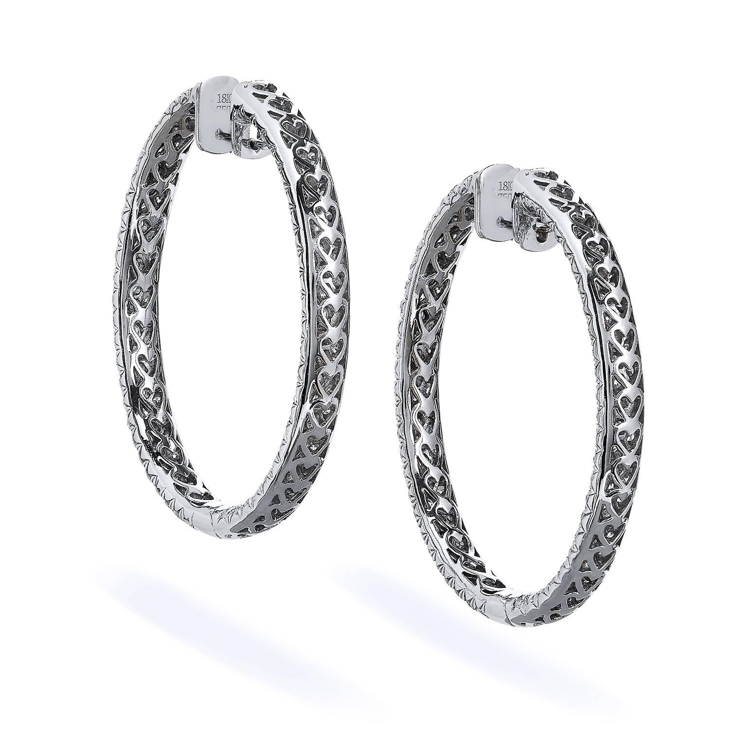 7.70 carat of diamonds pave set (G/H/VS2/SI1) and arranged inside and out in triple rows are affixed within 18 karat white gold in these striking hoop earrings. For added distinction and ornamentation, hearts are embossed on the back side of each