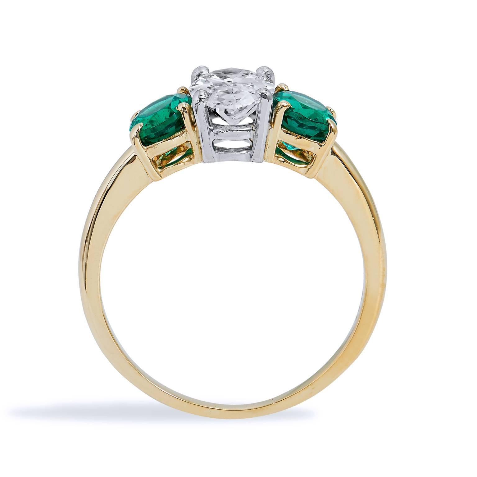 Make this previously loved Tiffany & Co. platinum and 18 karat yellow gold three oval diamond and emerald ring- an everyday expression of luxury, yours. This ring features a 1.05 carat oval diamond at center (F/WS2; GIA #6183239317) with two