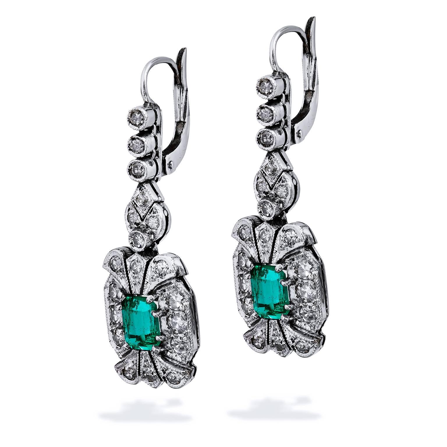 18 karat palladium, emerald, and diamond meld together to tell a story of romance, elegance and beauty in these previously loved drop earrings. Two emeralds, with a total weight of 1.15 carat, are prong set and are enveloped by 0.75 carat of pave