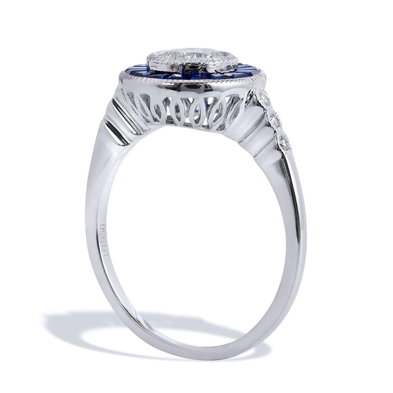 Crafted in platinum, this ring features a 0.63 carat I/SI1 graded Round Brilliant cut diamond set at center (GIA#6177461723) surrounded by 0.90 carat of caliber cut sapphires. The ring features a thin shank for a very soft and feminine feel that is