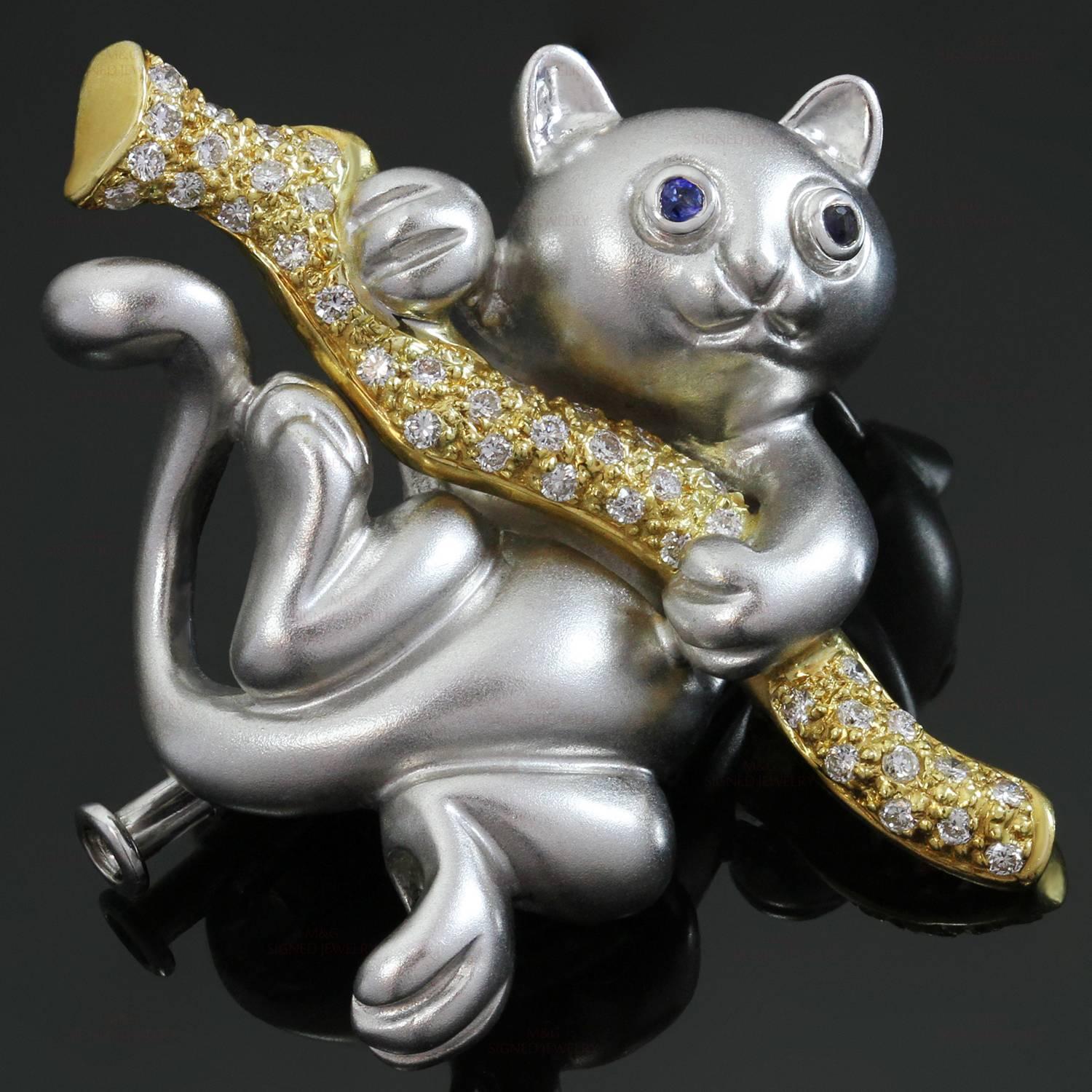 This stunning pendant brooch features a whimiscal cat with faceted blue sapphire eyes and an 18k matte white gold body, suspended from an 18k yellow gold branch set with brilliant-cut round diamonds of an estimated 0.33 carats. Made in United States