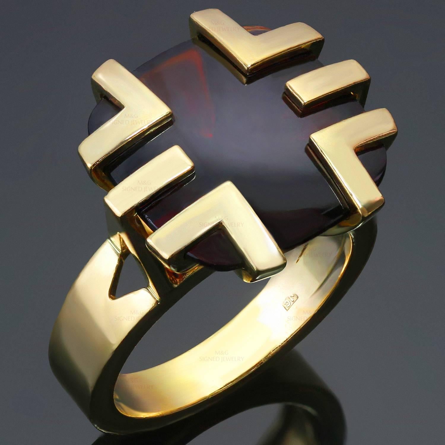 This gorgeous Cartier cocktail ring is crafted in 18k yellow gold and features a cabochon garnet set in a geometric crown. The 14.7mm x 14.9mm buff-top cushion-shaped garnet has dark red color with brownish tones, a fairly good transparency with