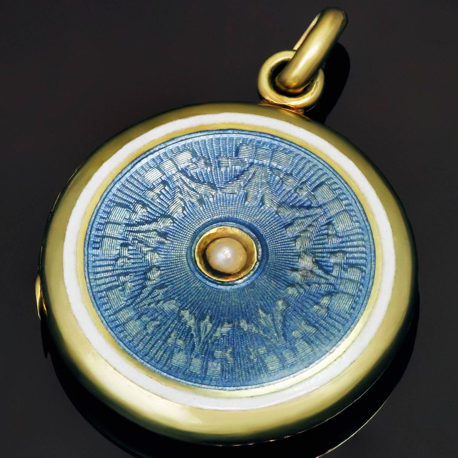 This beautiful circa 1910s  Art Nouveau round locket pendant is crafted in 14k yellow gold and displays a refined neoclassical design accented with translucent baby blue enamel shimmering over an elaborate engraved guilloche pattern  outlined and