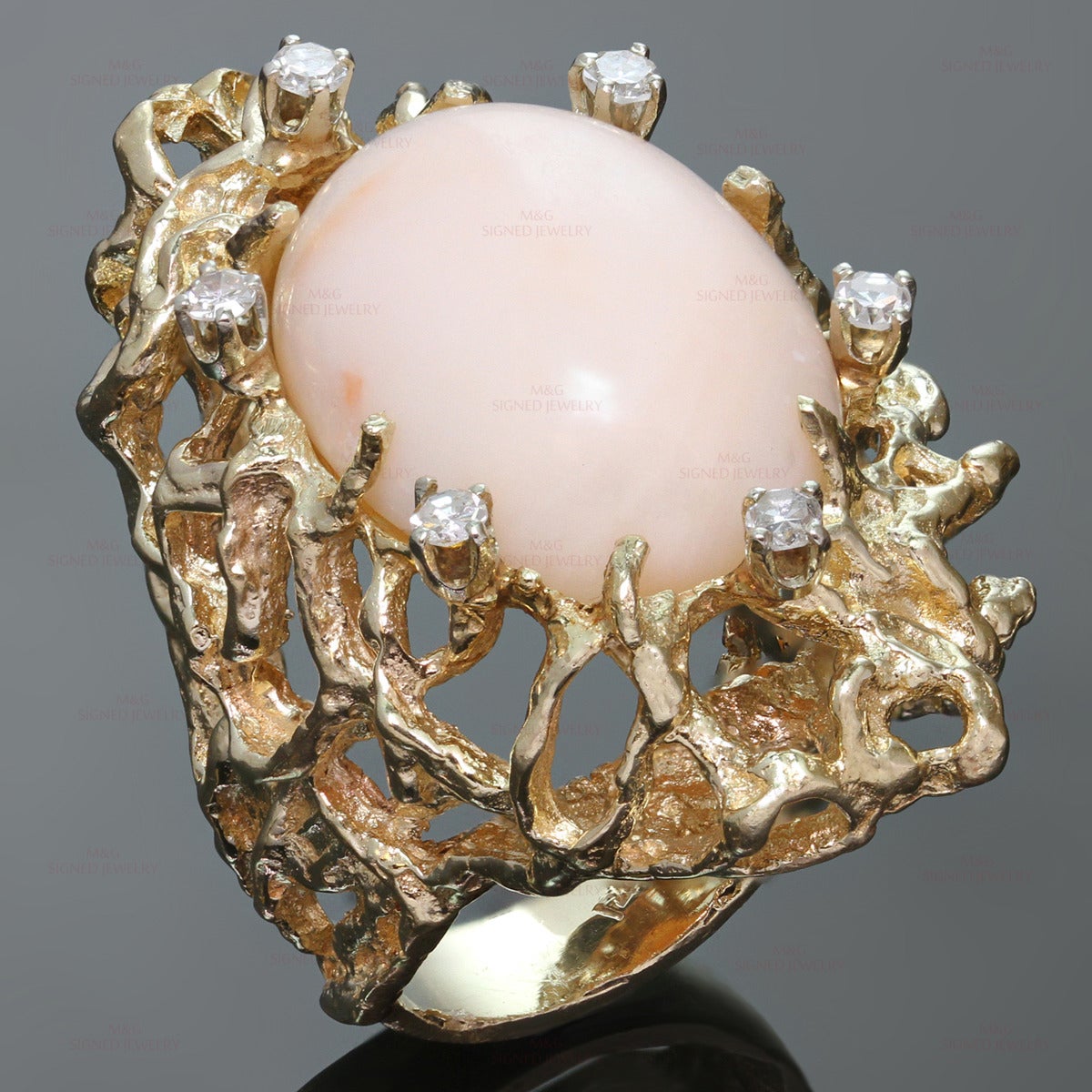 This stunning cocktail ring is crafted in 14k hammered yellow gold and set with a natural pink oval angel skin coral accented with 6 round-cut H-I VS1-VS2 diamonds of an estimated 0.36 carats. Made in United States circa 1960s. Measurements: 1.41