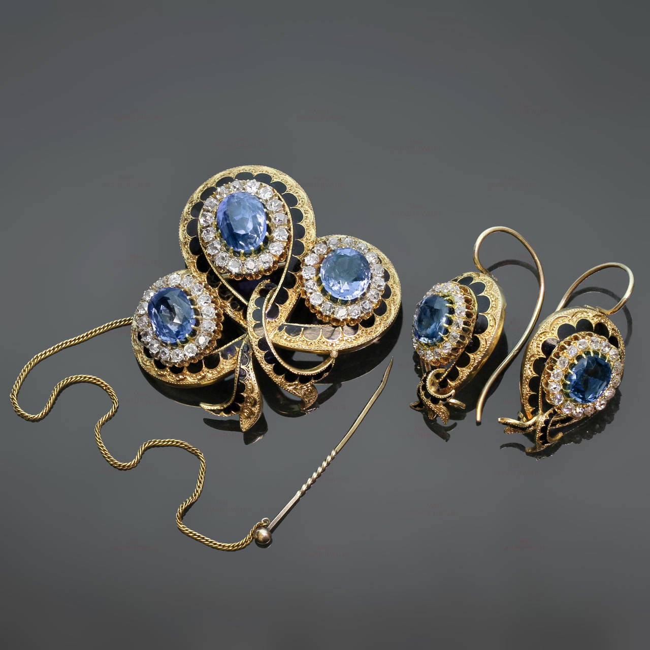 This magnificent Victorian jewelry suite consists of a pendant-brooch and a pair of earrings featuring an intricate filigree design hand-crafted in 18k yellow gold and contrasted with black enamel. This suite is beautifully prong-set with natural