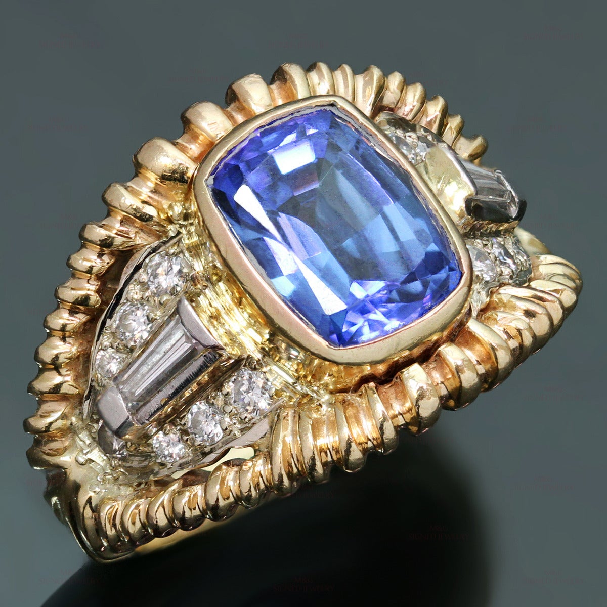 This gorgeous ring is crafted in 14k yellow & white gold and set with a faceted royal blue tanzanite of an estimated 4.0 - 5.0 carats, surrounded with baguette and round-cut H-I VS2-SI1 diamonds of an estimated 0.62 carats. Made in United States