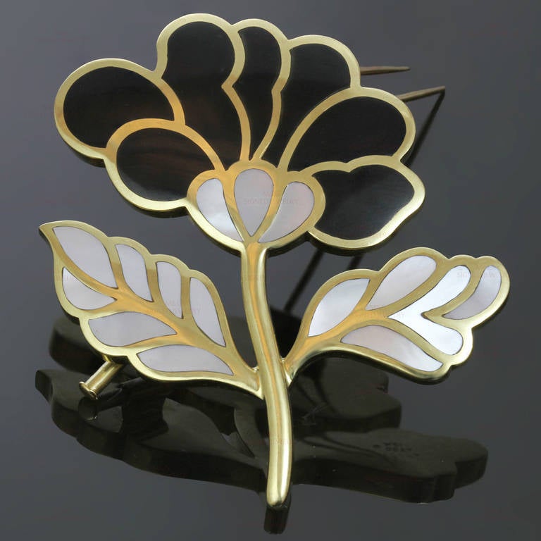 This gorgeous Tiffany & Co. brooch features a flower-shaped design in a stunning contrast of black jade petals and mother-of-pearl leaves inlaid in 18k yellow gold. Measurements: 2.16" (55mm) width, 2.24" (57mm) length.
