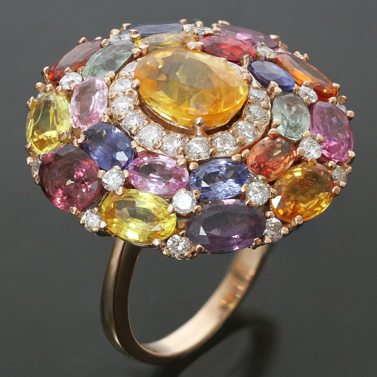This modern Italian ring is made in 18k rose gold and set with a stunningly colorful array of natural faceted oval sapphires - 20 sapphires of an estimated 14.5 carats, 1 center sapphire of an estimated 2.5 carats, and 30 diamonds of an estimated