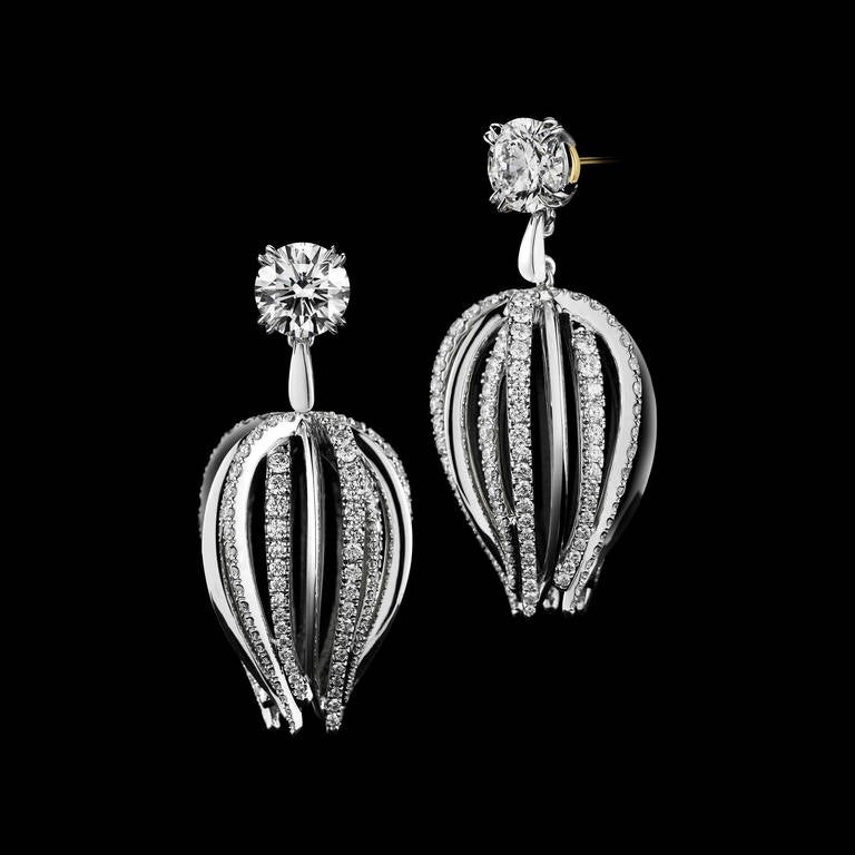 A pair of dangling curved-waist Diamond earrings are suspended by GIA certified Ideal-cut Round Brilliant Diamonds. Carat weight, color and clarity is 1.04 and 1.01 carats, GVS2. Earrings also feature three hundred fifty Diamonds in Alexandra Mor's