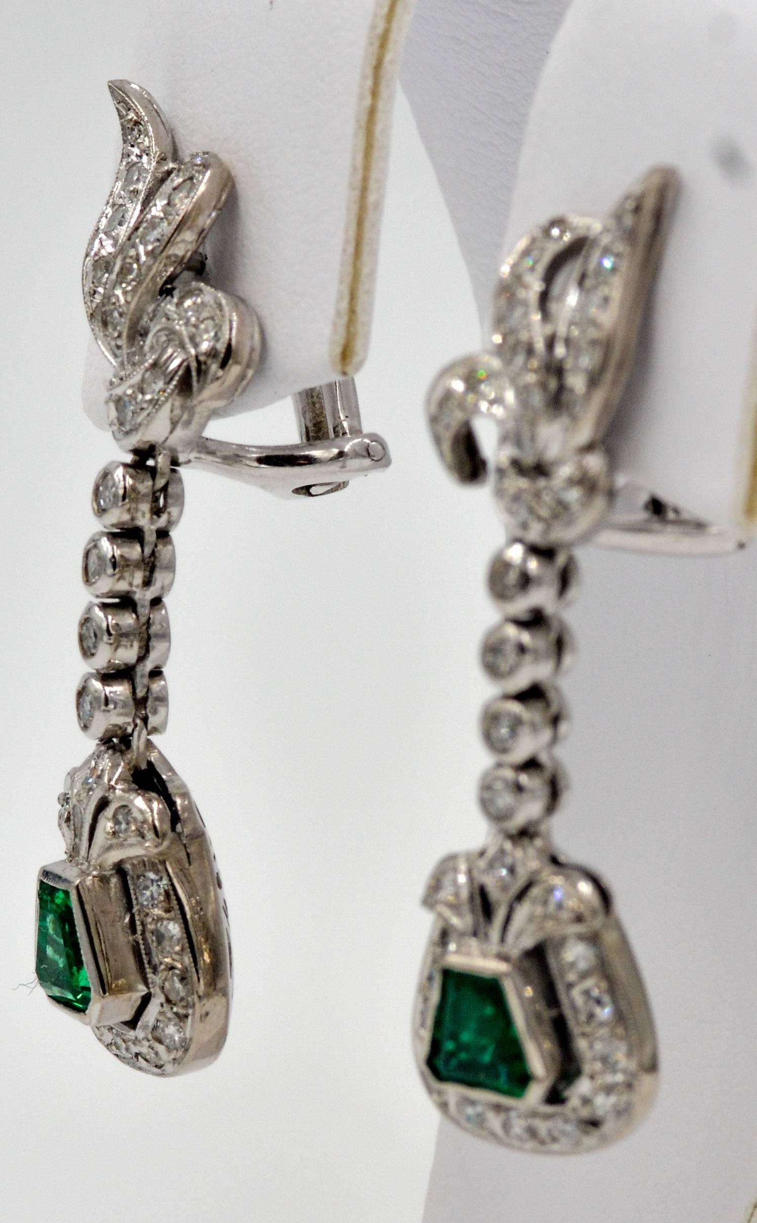 This classic Retro style pair of earrings features a beautifully matched pair of shield cut emeralds that have an approximate combined weight of 0.88 carats. The intensity of the green in the emeralds is expertly contrasted with a halo, drop link,