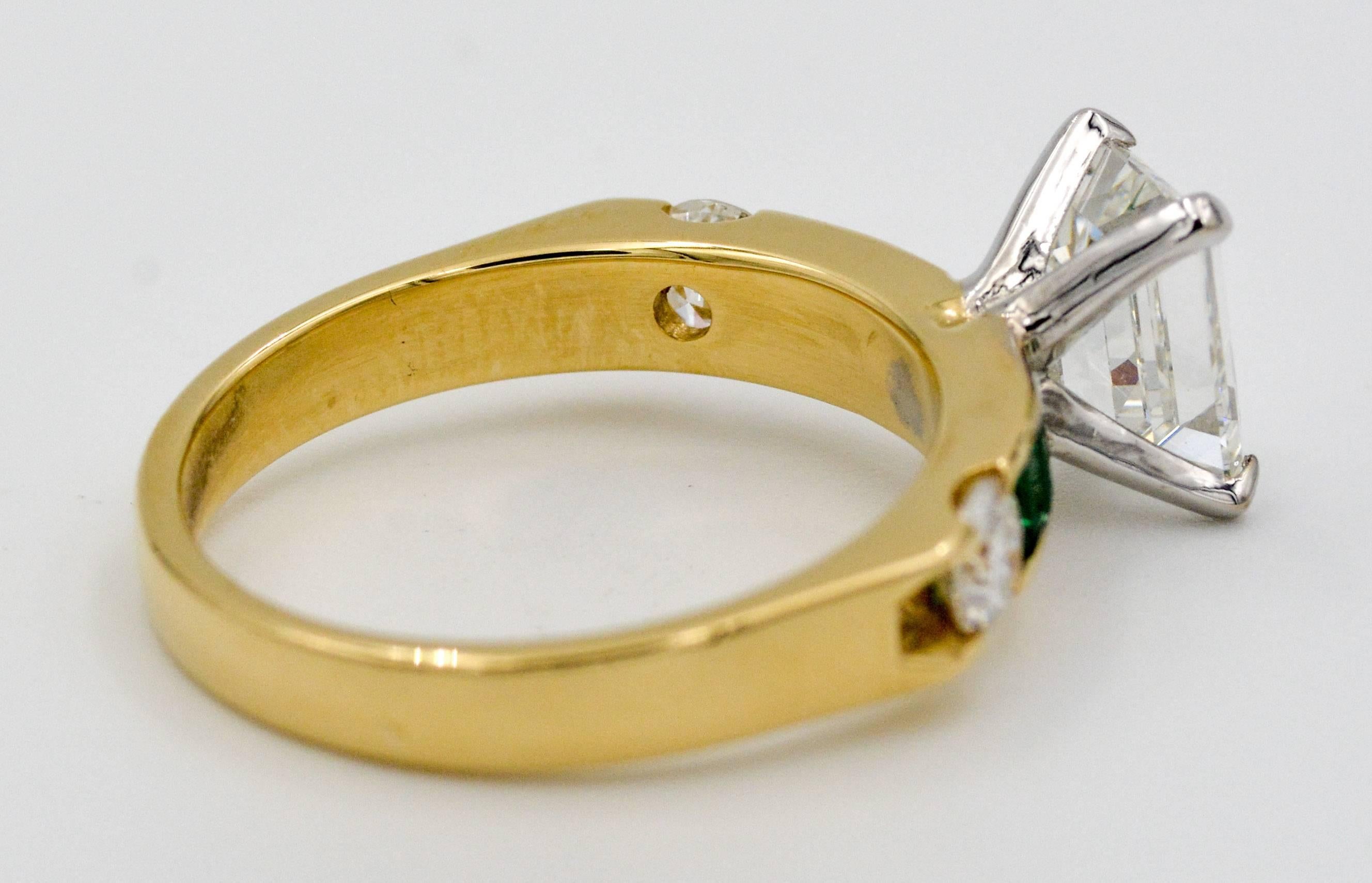 The dynamic simplicity of an emerald cut diamond surrounded by emeralds creates an engagement ring like none other. This 18kt yellow gold ring features a stunning 1.33 ct emerald cut diamond (J color and VS2 clarity), in a setting that tapers to a