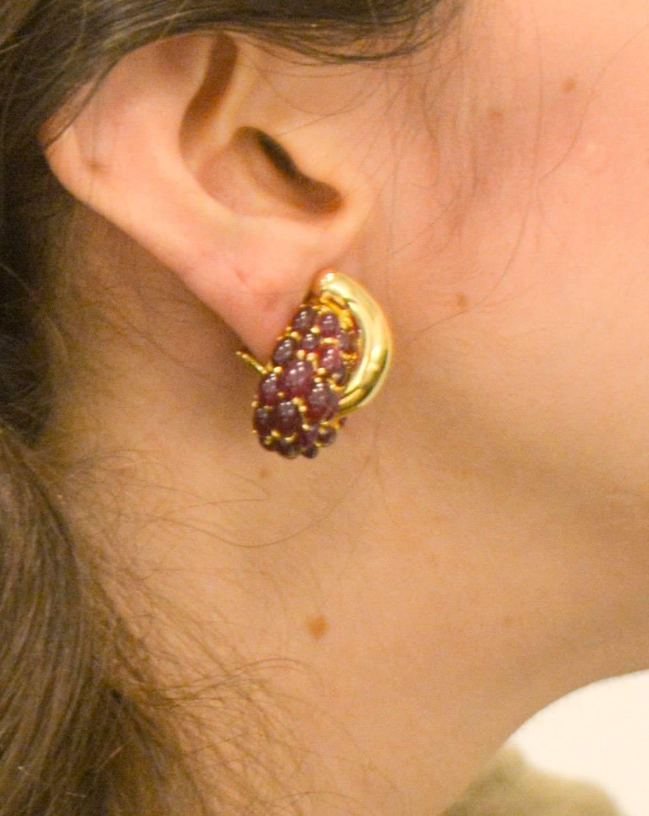Seaman Schepps crafted these opulent 18kt yellow gold ruby earrings in his signature style with bright bold cabochon red rubies cascading down one side and swirling around a bold gold crescent shape.  The earrings are set with a total of 46 oval