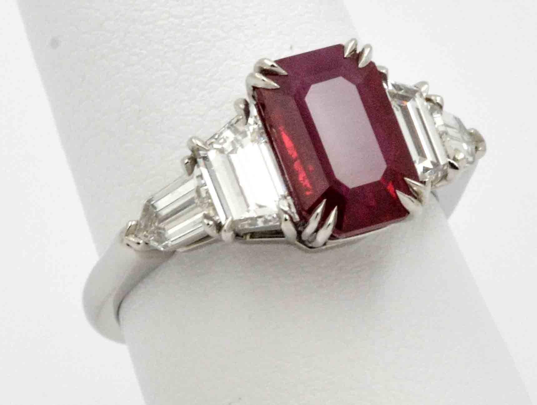 Cool sophistication and a touch of color in this stylish custom vivid red 3.01 carat emerald cut Burmese Ruby platinum engagement ring. Accenting this elegant ruby are two matched trapezoid cut diamonds that have a combined weight of 0.84 carats (E