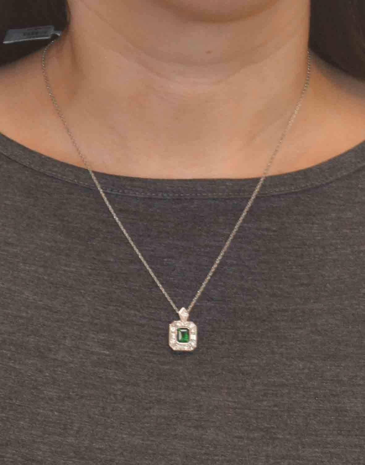 This amazing platinum, diamond, and Emerald pendant features a 1.11 carat  vivid green emerald cut emerald bezel set in the center of the pendant.  This beautiful green emerald is artistically bordered by a channel set halo of baguettes and round