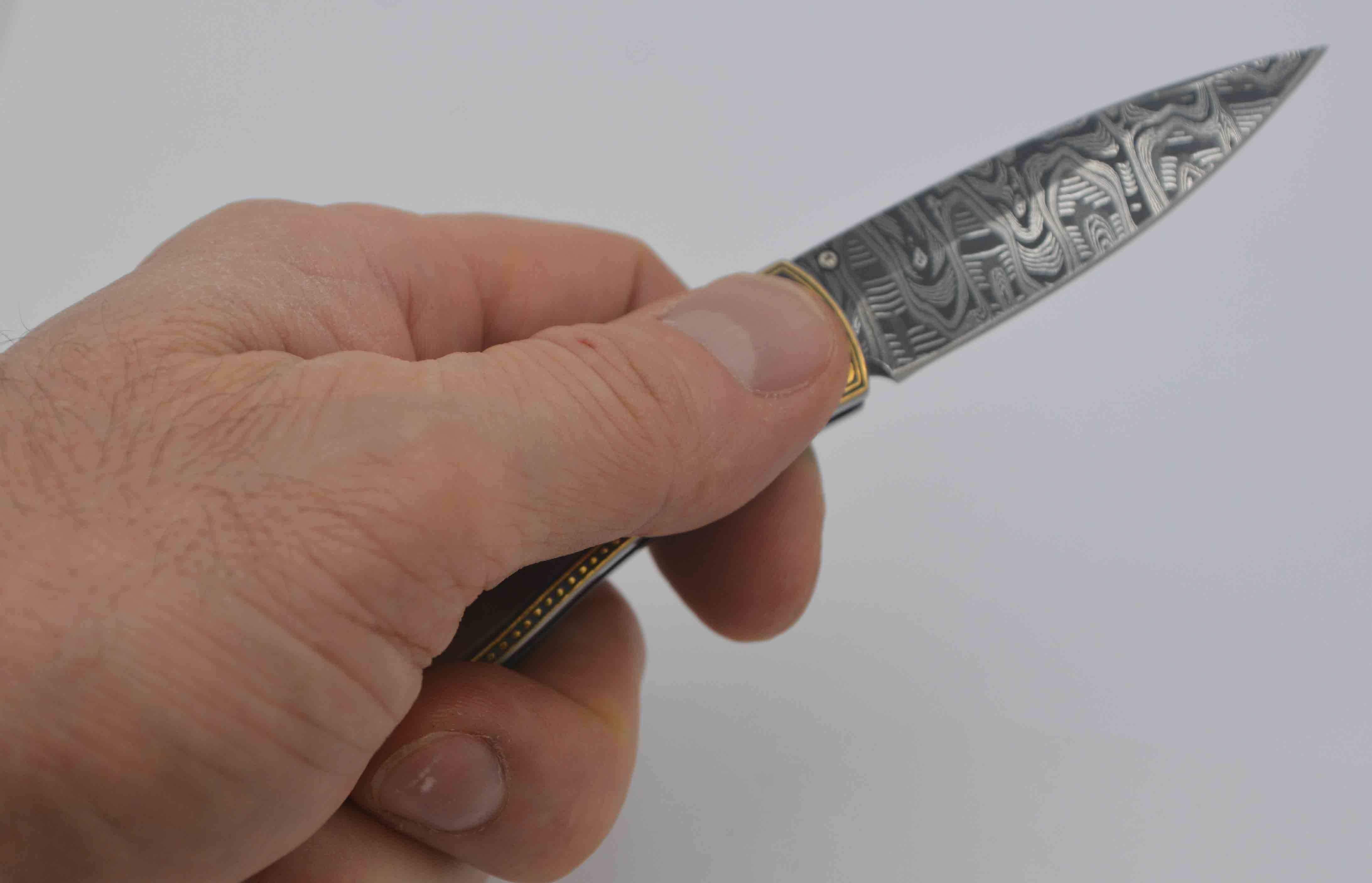 This amazing William Henry knife is crafted with a spear point Damascus steel blade with a leopard skin pattern.  William Henry finished the handle to feature an incredible black mother of pearl inlay surrounded by an artful 24kt yellow gold