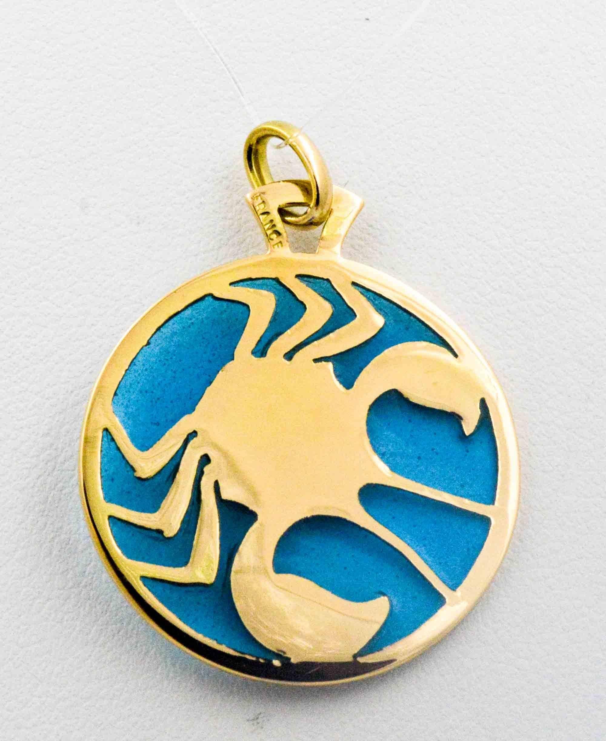 On a background of blue enameled glass is featured the Cancer zodiac sign. Cancer is accented with 18 karat yellow gold  and its body is amber enameled glass. The master craftsman expertly created this Plique a Jour handcrafted glass enameling in