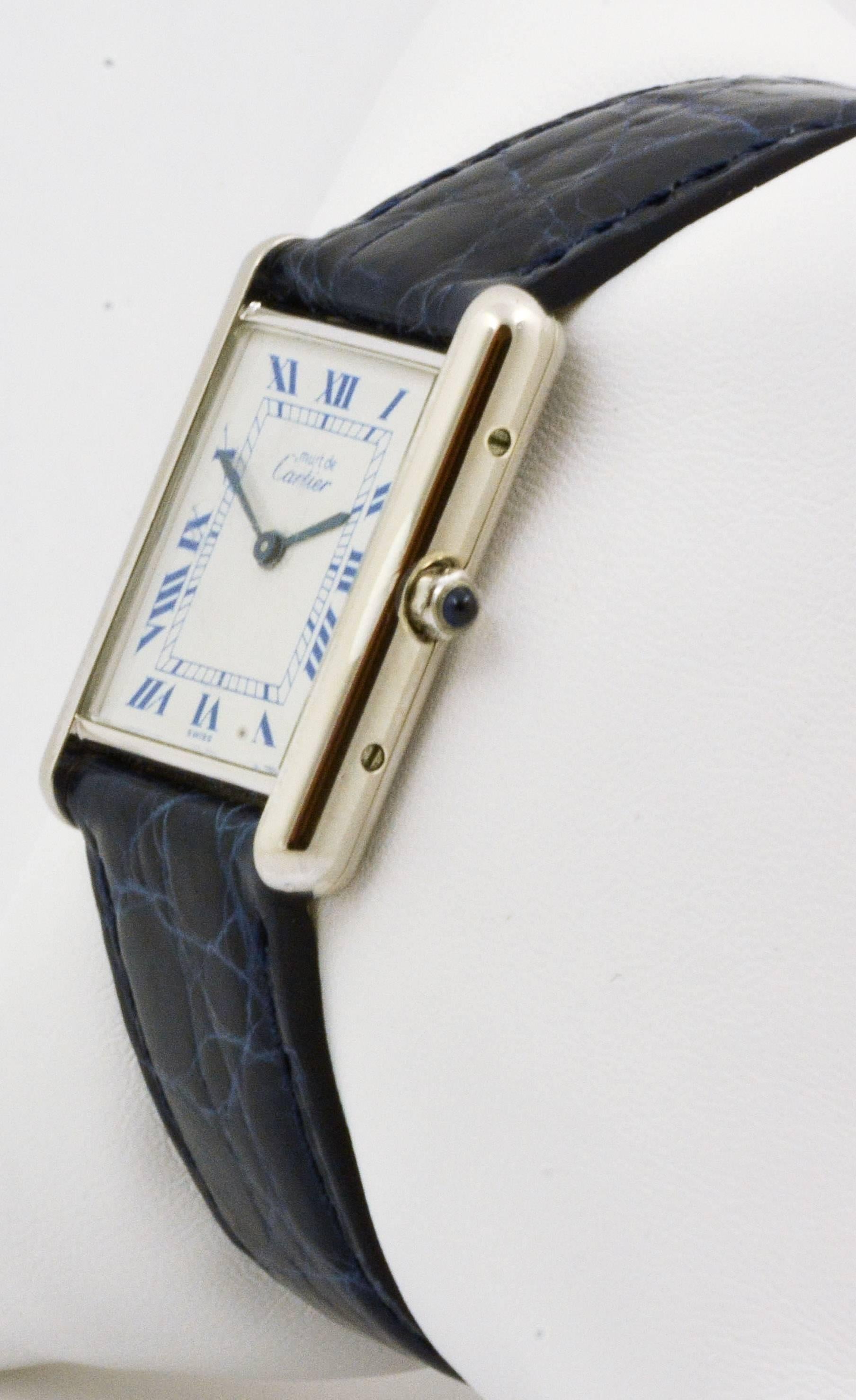 Dieser Circa 1987 Sterling Silber Cartier Tank Uhr ist in gutem Zustand.  Sie hat ein 20 x 28 mm großes Gehäuse, ein weißes Zifferblatt mit blauen römischen Ziffern, ein Quarzwerk und Saphirglas.  Die Uhr wird mit einem neuen marineblauen Lederband