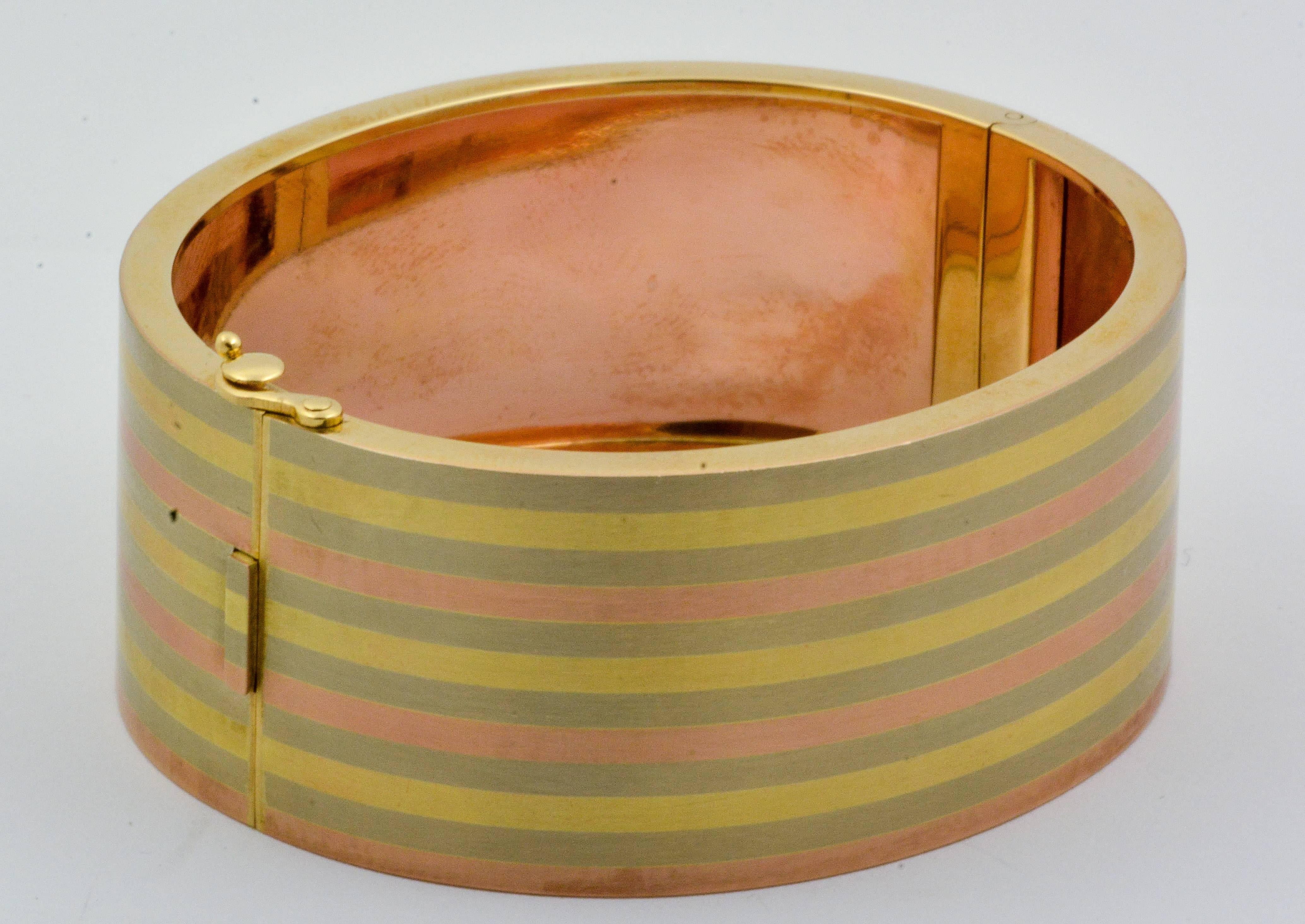 This beautiful hinged bangle bracelet makes a fashion statement with its unique 14kt stripes of yellow, rose, and white gold. Its entire surface is satin finished and flat across its 25.3mm width. The bangle features a hidden hinge to keep its