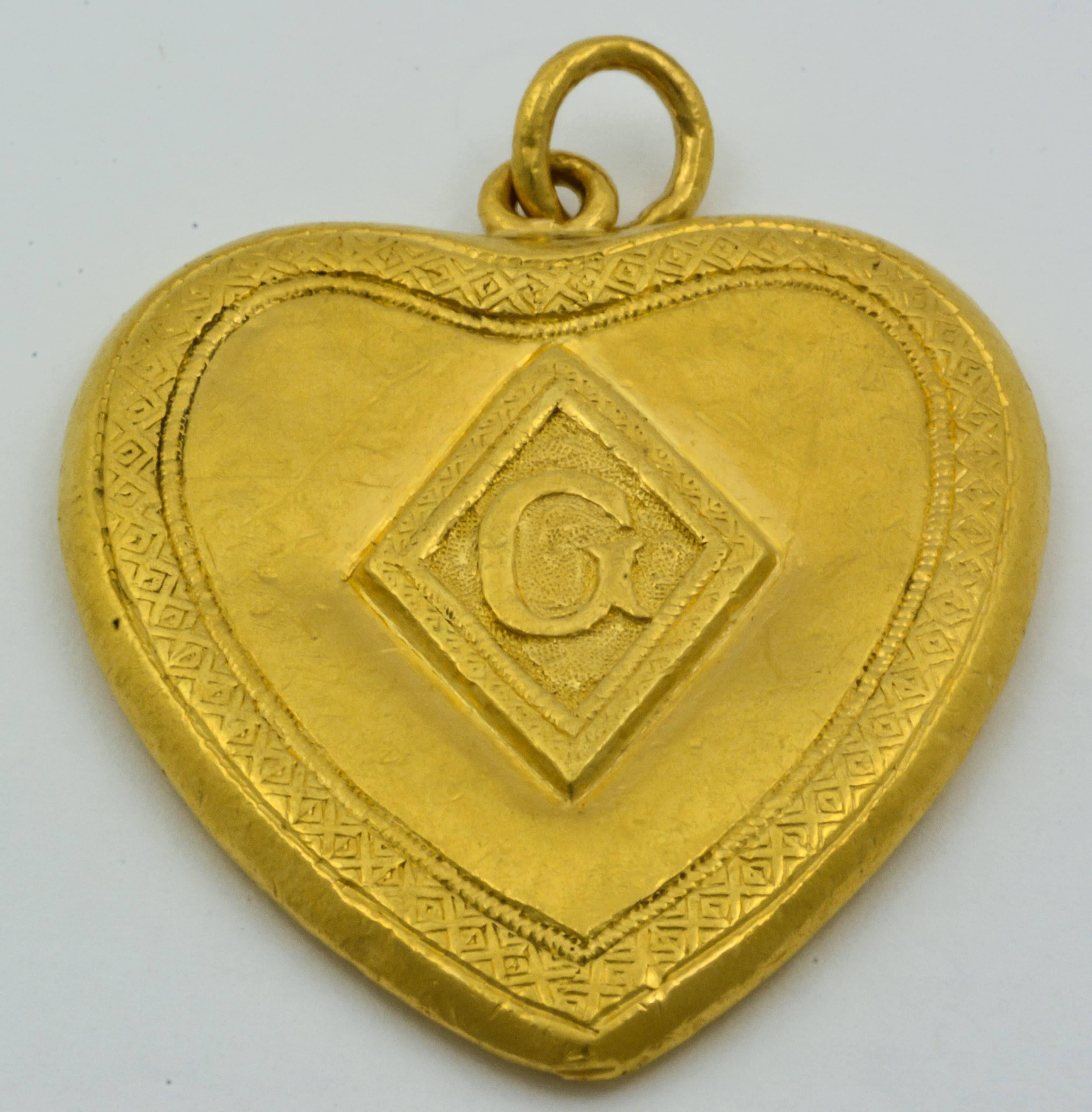 A beautiful flower and vine design is delicately carved into the antique gold of this heart-shaped pendant. An attractive monogram styled “G” is centered on the back of the heart. This Art Nouveau piece measures 37.33mm tall, 32.55mm wide, and 3.5mm