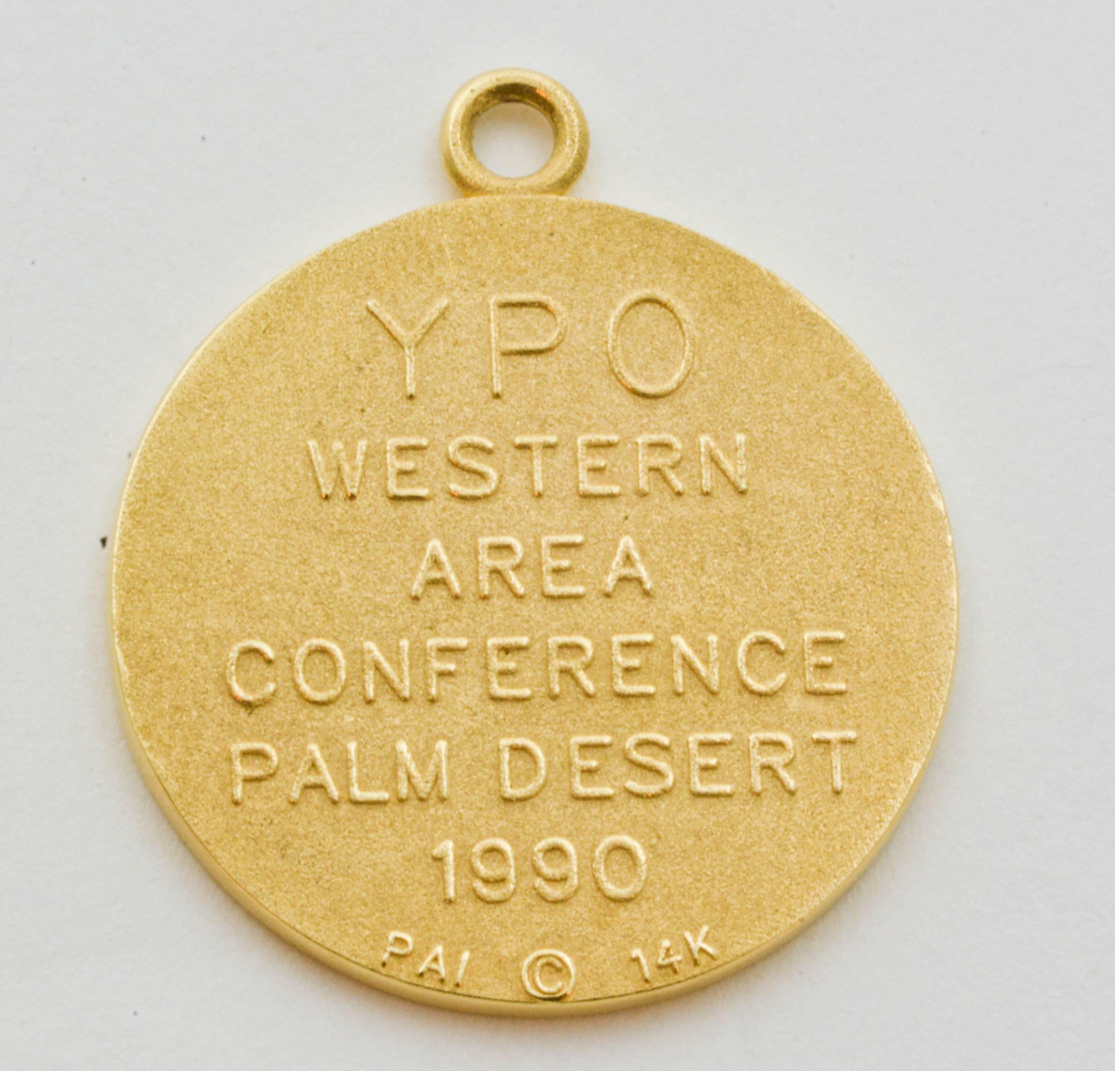 This Palm Desert charm is crafted  in 14 karat yellow gold and features a whimiscal stylized desert golf course theme. The back is embossed with the words “YPO Western Area Conference Palm Desert 1990.” Measuring 21.8mm in diameter and 1.54mm thick,