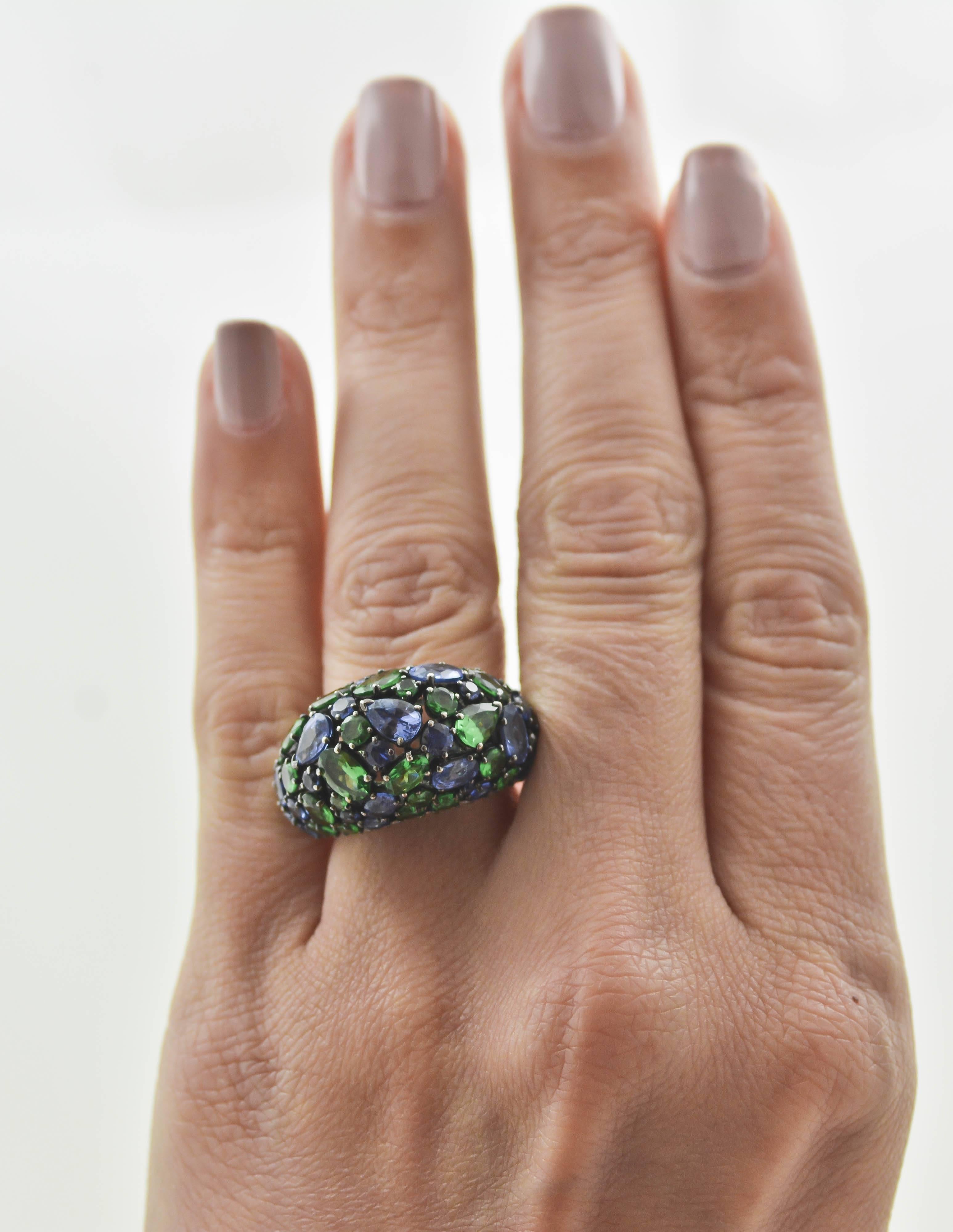 18kt white gold sets the stage in this artistic, high domed, multi-gem ring. 27 blue sapphires (4.97 carats), 31 tsavorite garnets (31.4 carats) and 34 diamonds (0.53 carats; clarity VS color G) contrast flawlessly in this colorful masterpiece. The