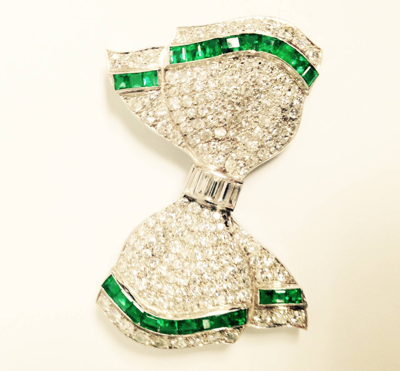 Platinum Art Deco Geometric Bow Brooch Consisting Of 8 Carats Of Superior quality full cut diamonds and further embellished with 2.50 cts of beautiful quality custom cut calibre cut colombian emeralds centering 6 high quality very white baguette cut
