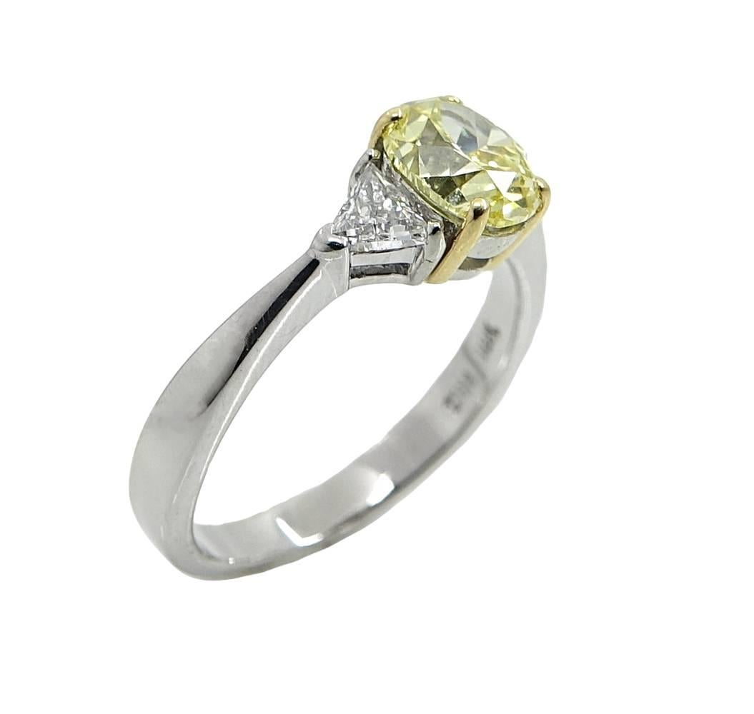 This Sweet, Yet Simple 18K White Gold and Yellow Gold Engagement Ring Has A Beautiful Oval Cut Brilliant Fancy Intense Yellow Diamond In The Center Weighing A Total Carat Weight Of 1.08 Carats, VS1 Clarity. (GIA CERT: 14289989) Two Diamond Sit On