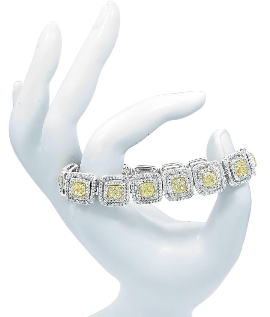 This 18k white gold tennis bracelet holds 14 cushion cut fancy yellow diamonds which equal 14.70cts with SI1-SI2 clarity. There are approximately 792 round brilliant cut colorless SI1 quality diamonds in the double halo surrounding each of the fancy