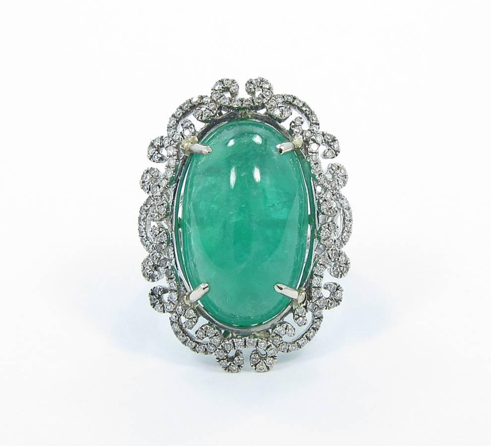 Center cabochon emerald weighs 20.45cts. It has a few surface reaching inclusions and measures 14mm x 23mm. Surrounding the emerald is approximately .98cts of round brilliant cut diamonds all securely prong set with a vintage style. Ring is