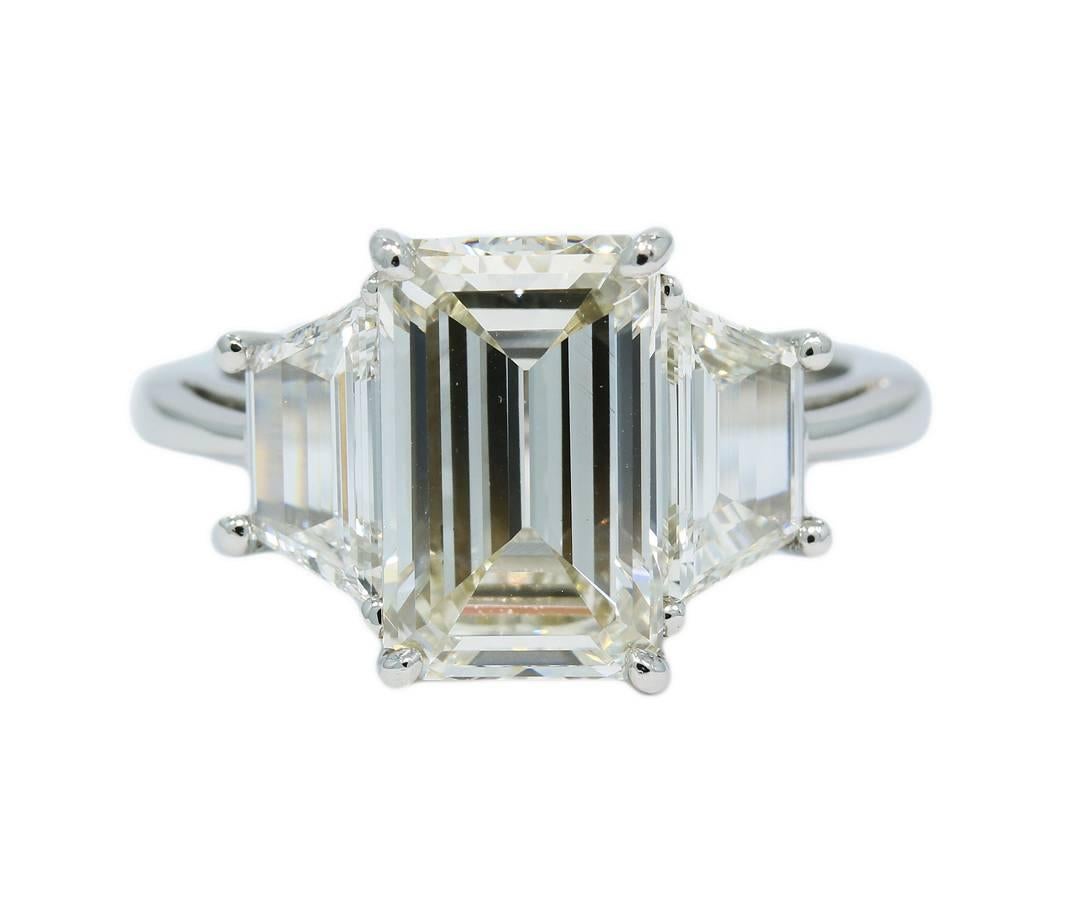 This beautiful 3 stone Diamond Engagement Ring holds a 3.06ct center emerald cut diamond that has a weight of 3.06cts with J color and VS1 in clarity. The two trapezoids on the side have a combined weight of 10.6cts with the same quality. All