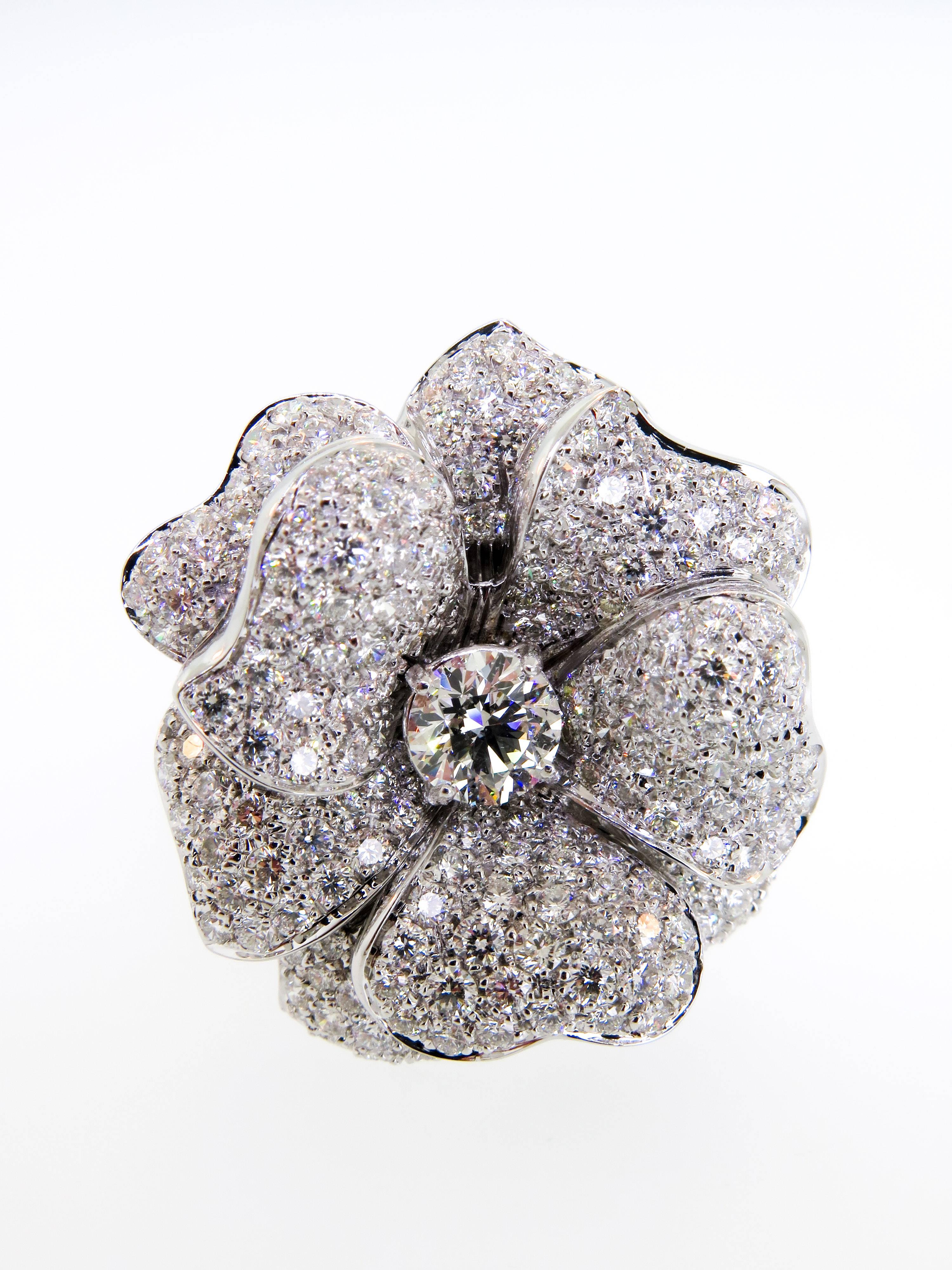 This charming Pavé diamond flower ring is centered by a larger round diamond weighing approximately 1.00ct  H/VS1 handcrafted in 18K white gold. The Diamond flower motif measures approximately 32mm in diameter (1.25 inches). Size 8.5